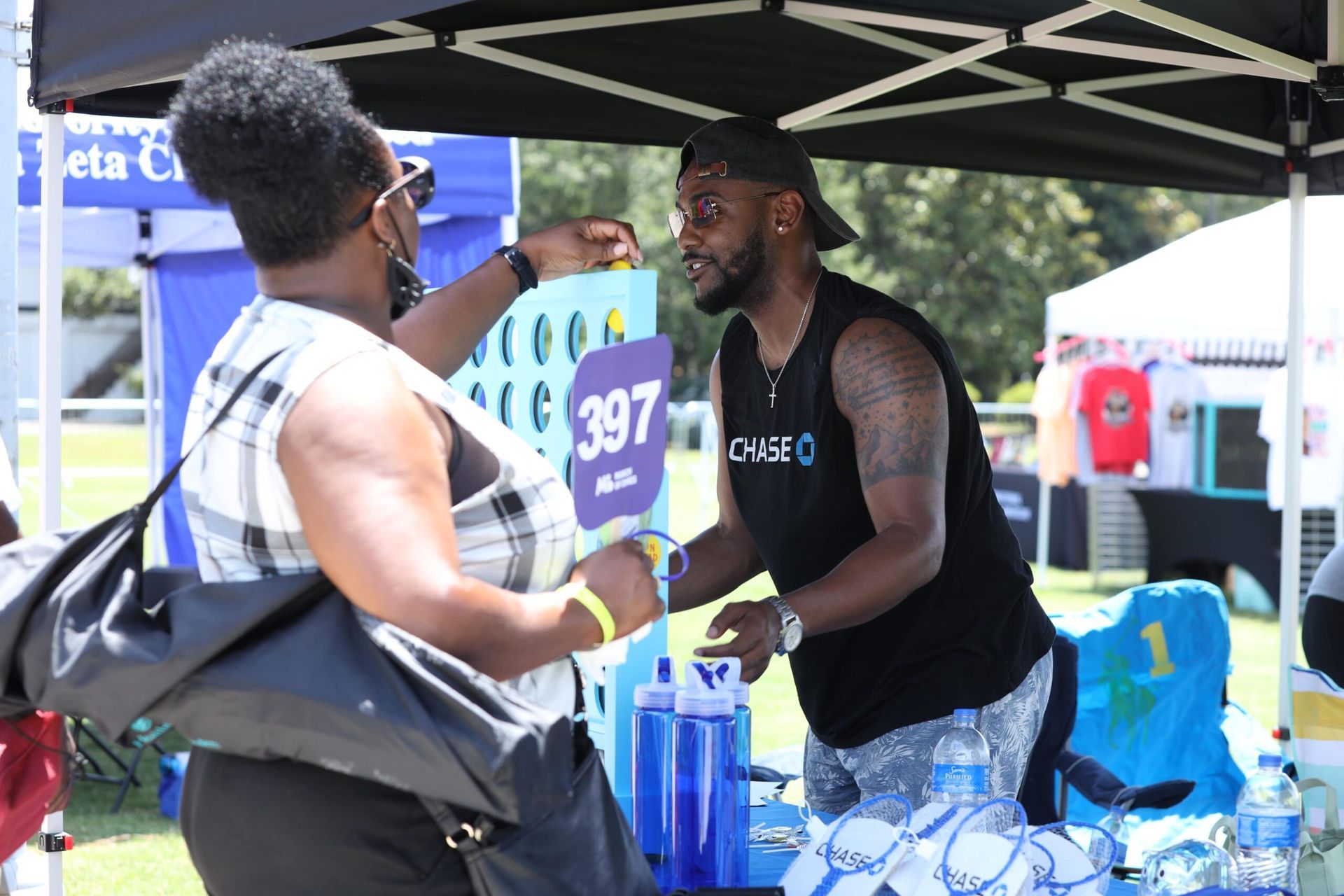 Two people talking at an outdoor booth under a black canopy, with water bottles on the table.