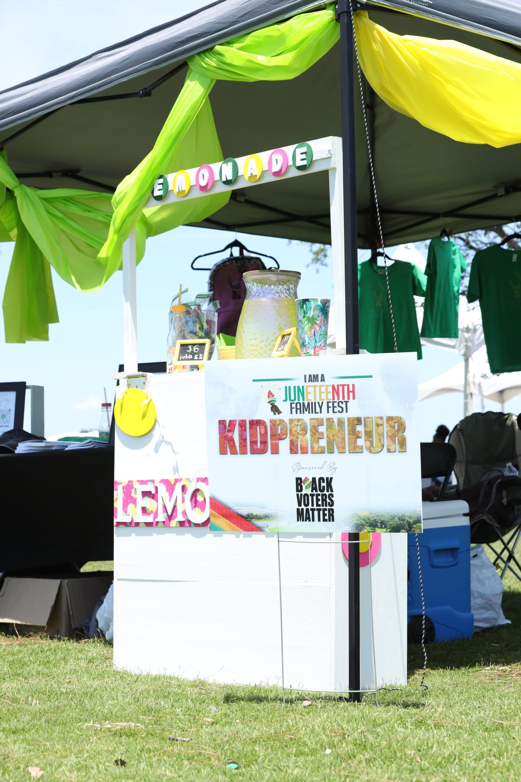 Outdoor food stall with a colorful canopy, sign reading “KIDPENET,” and items displayed on a table