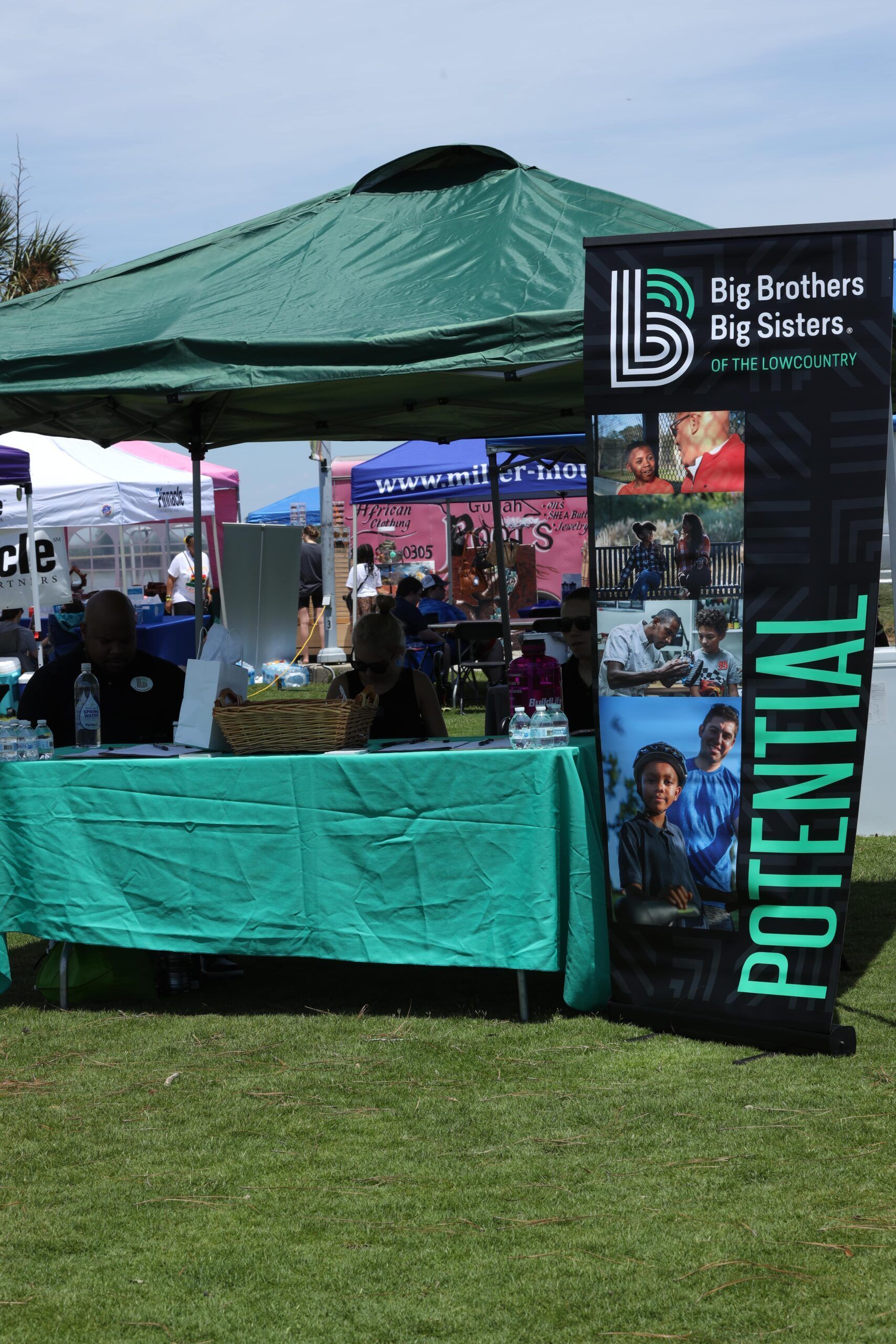 Big Brothers Big Sisters green tent booth at an outdoor fair, with “Potential” banner and table display