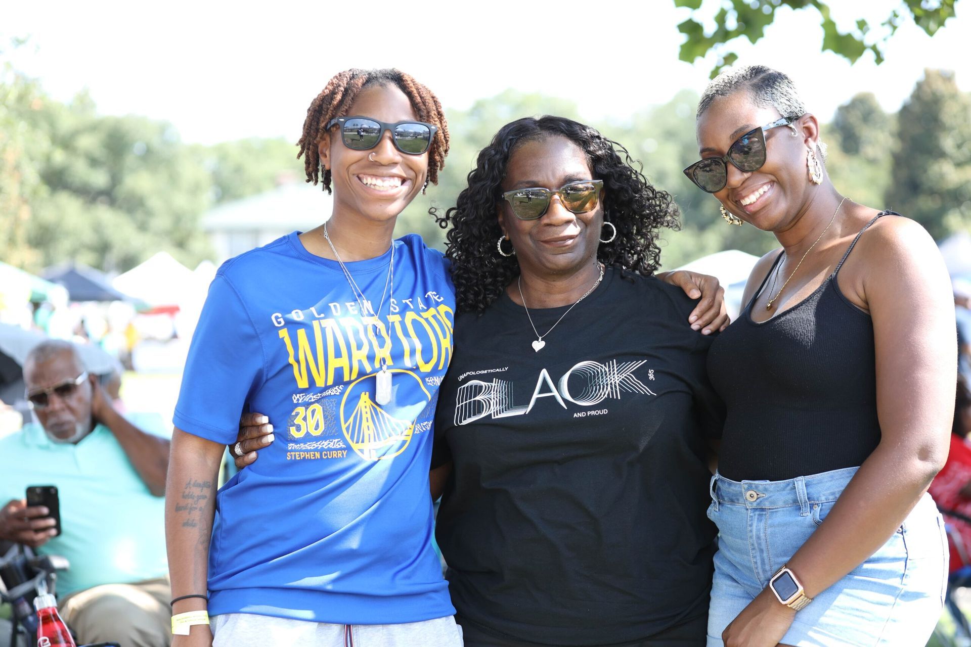 Three people smiling outdoors, wearing sunglasses and casual summer clothes.