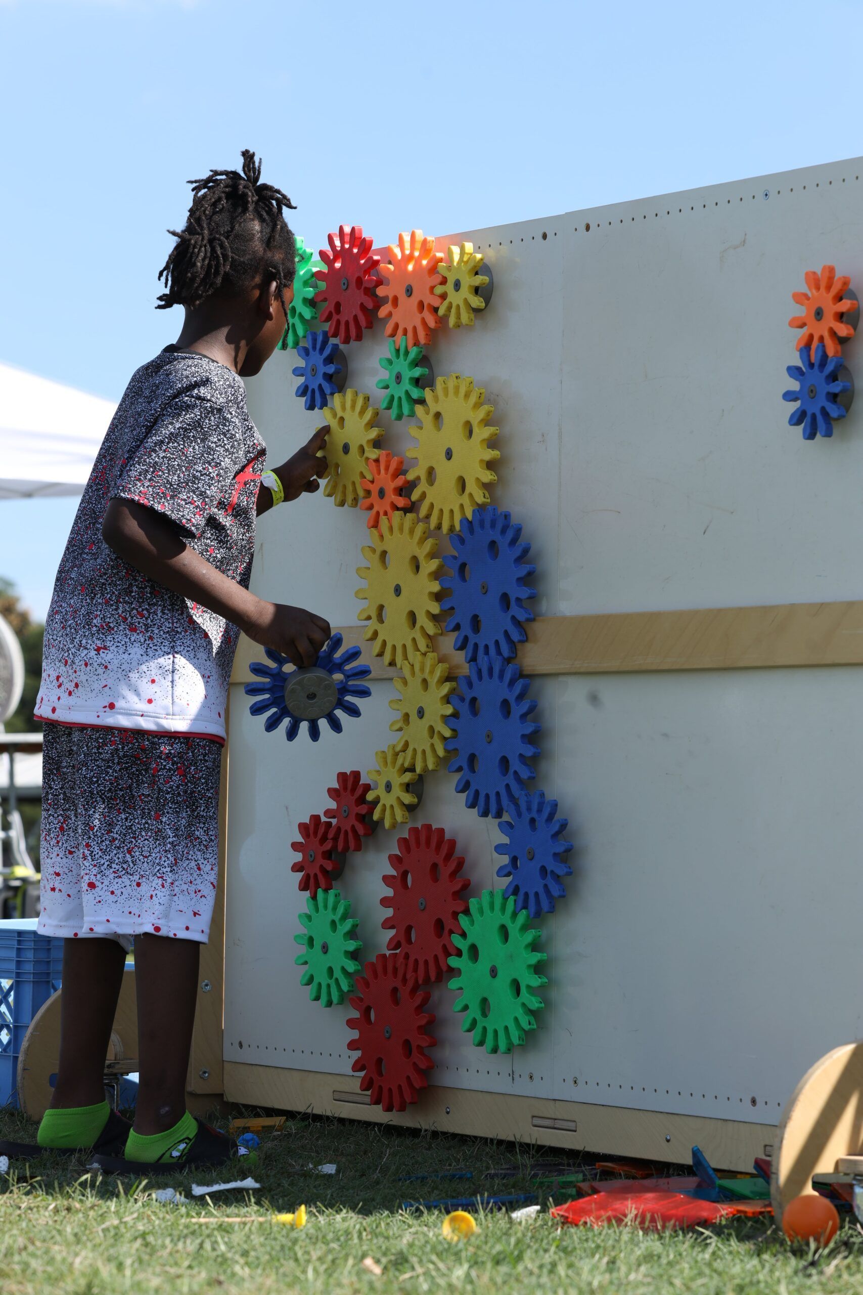 Person arranging colorful gear-shaped decorations on a vertical board outdoors