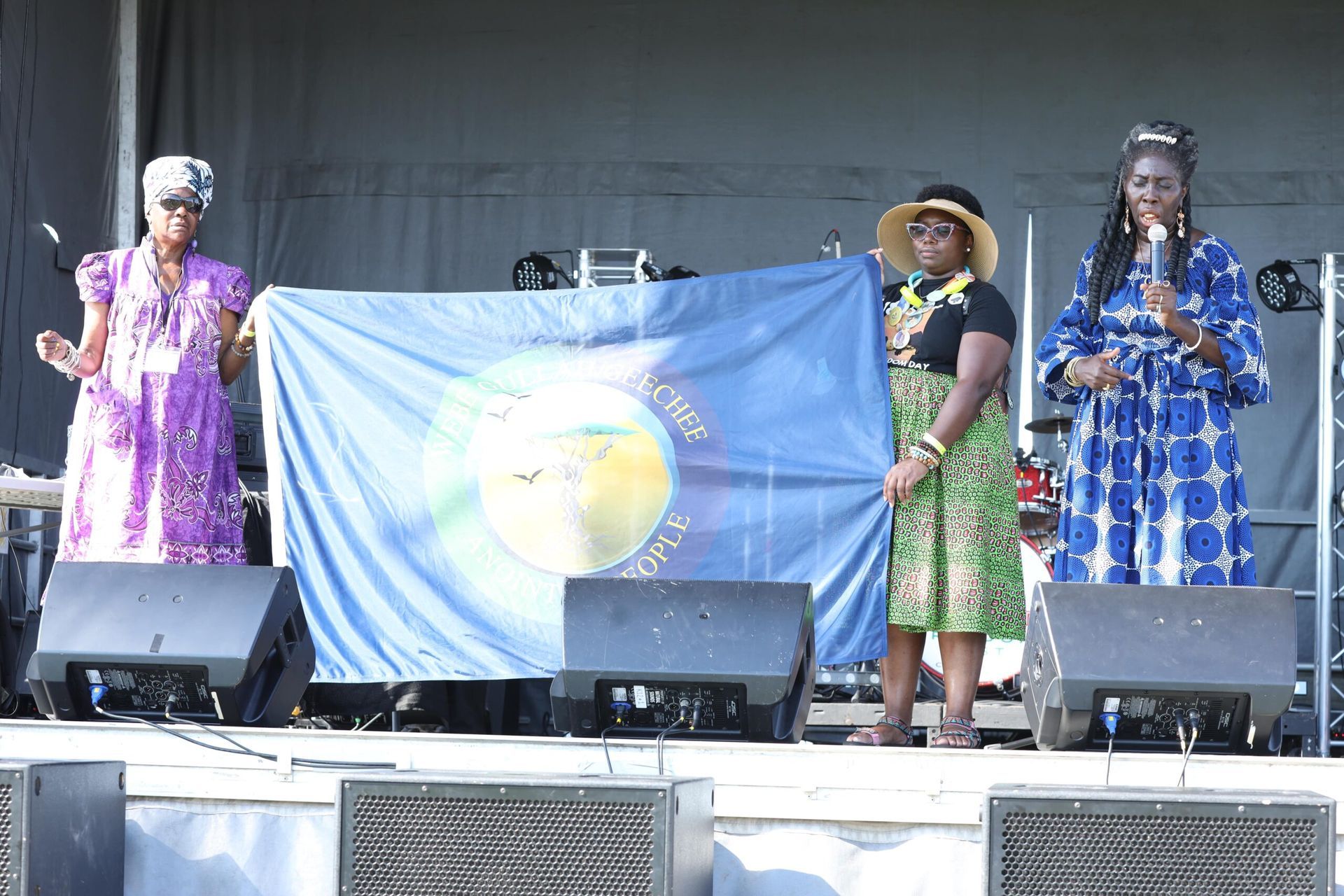 Four performers onstage holding a blue flag, with speakers in front of them.