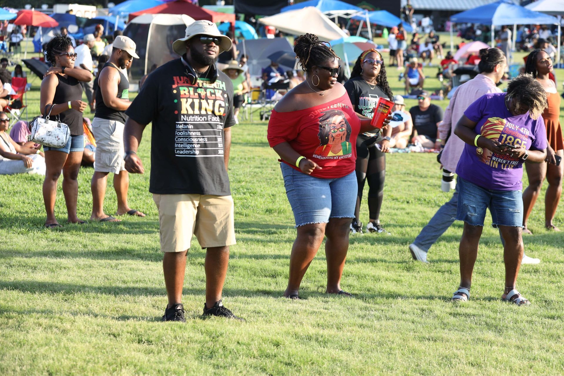 People dancing on a grassy field at an outdoor festival with colorful umbrellas and tents in the background