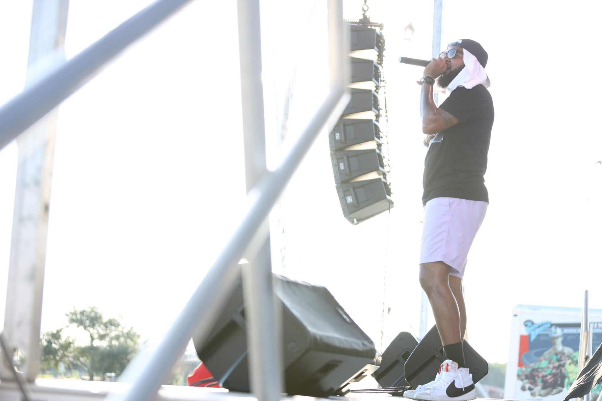Musician singing into a microphone on an outdoor stage beside a tall speaker stack