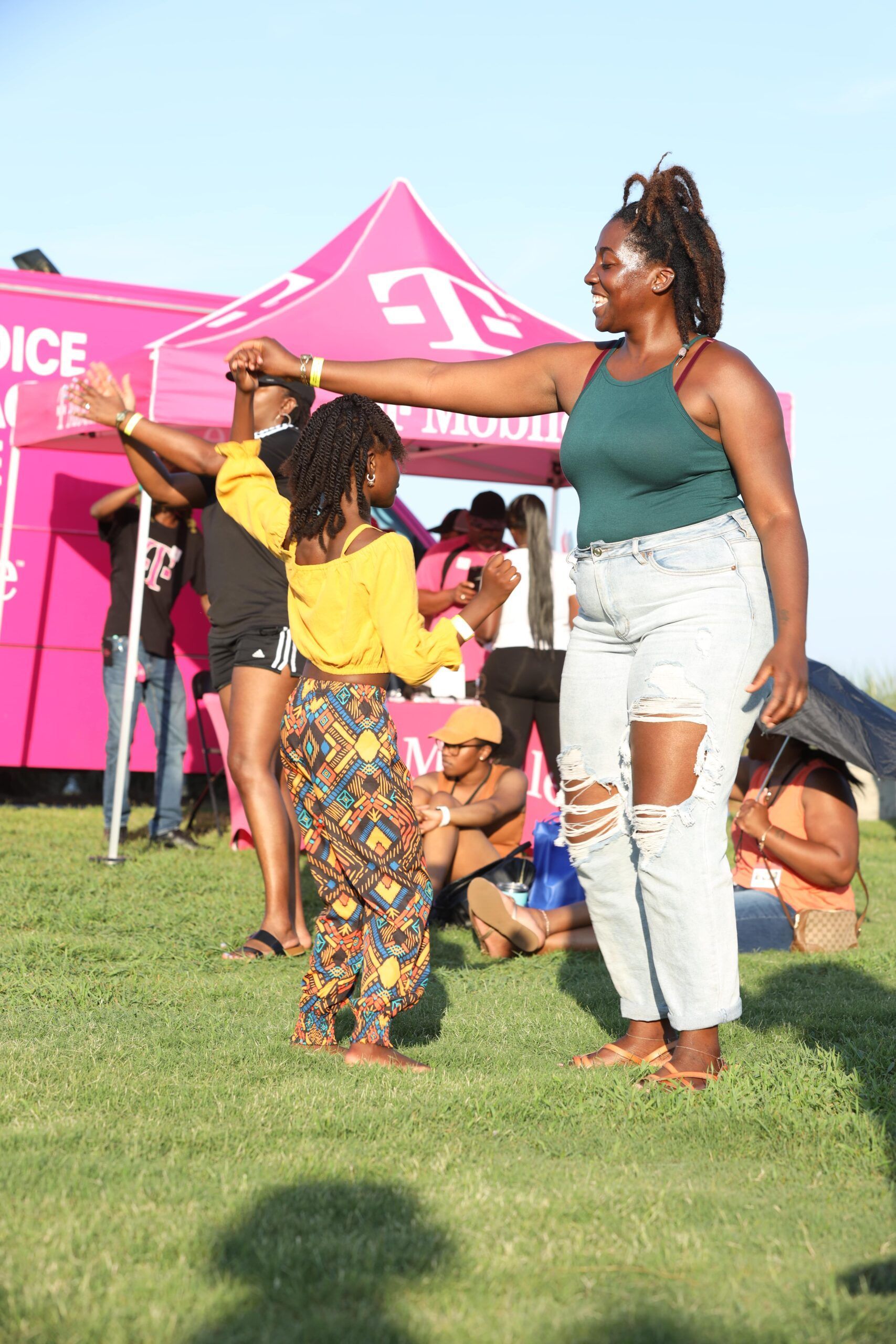 Two women dancing on grass beside a pink tent at an outdoor event.