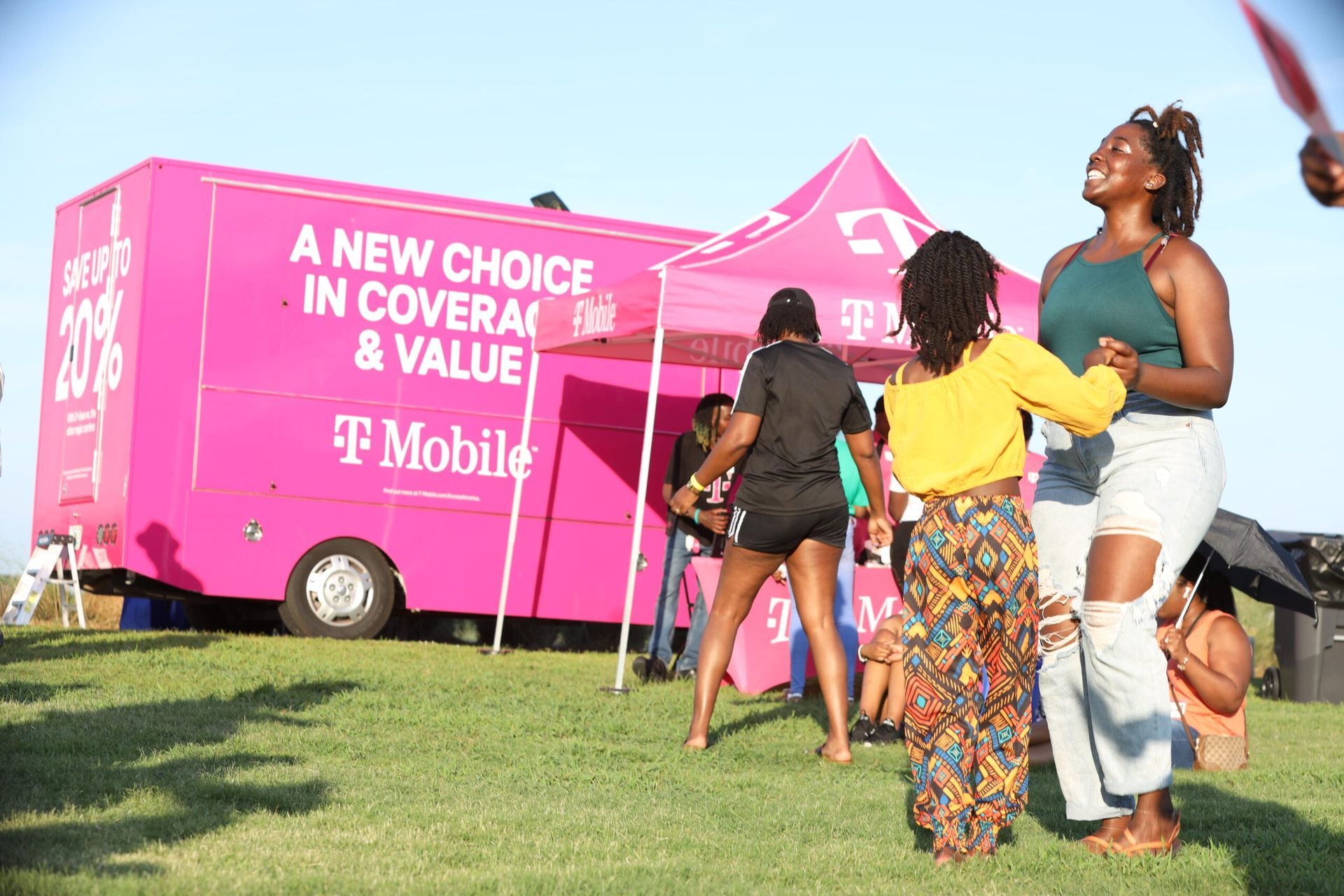 Pink T-Mobile truck at an outdoor event with people standing nearby on a grassy field