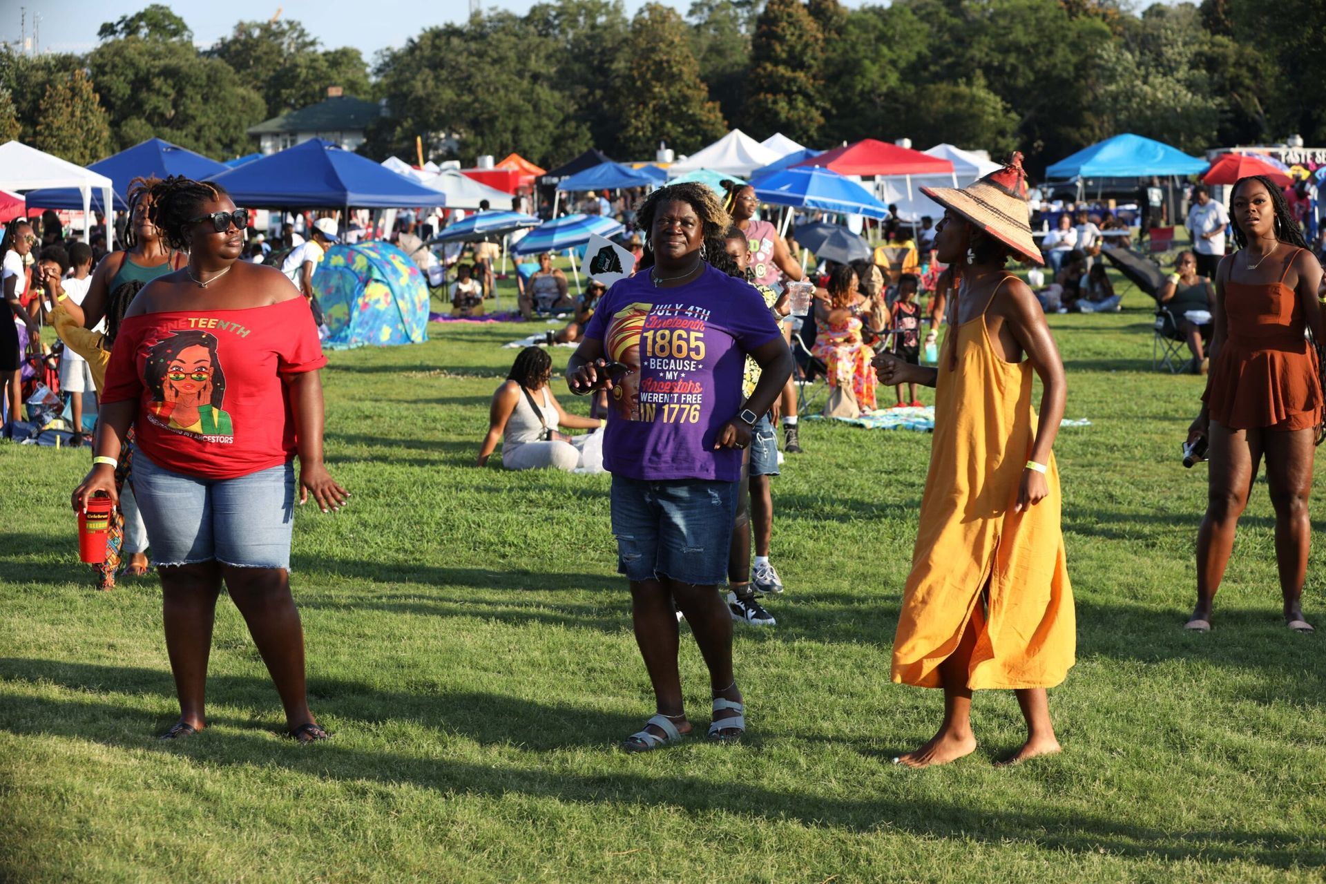 People walking on a grassy field at an outdoor festival with colorful tents in the background