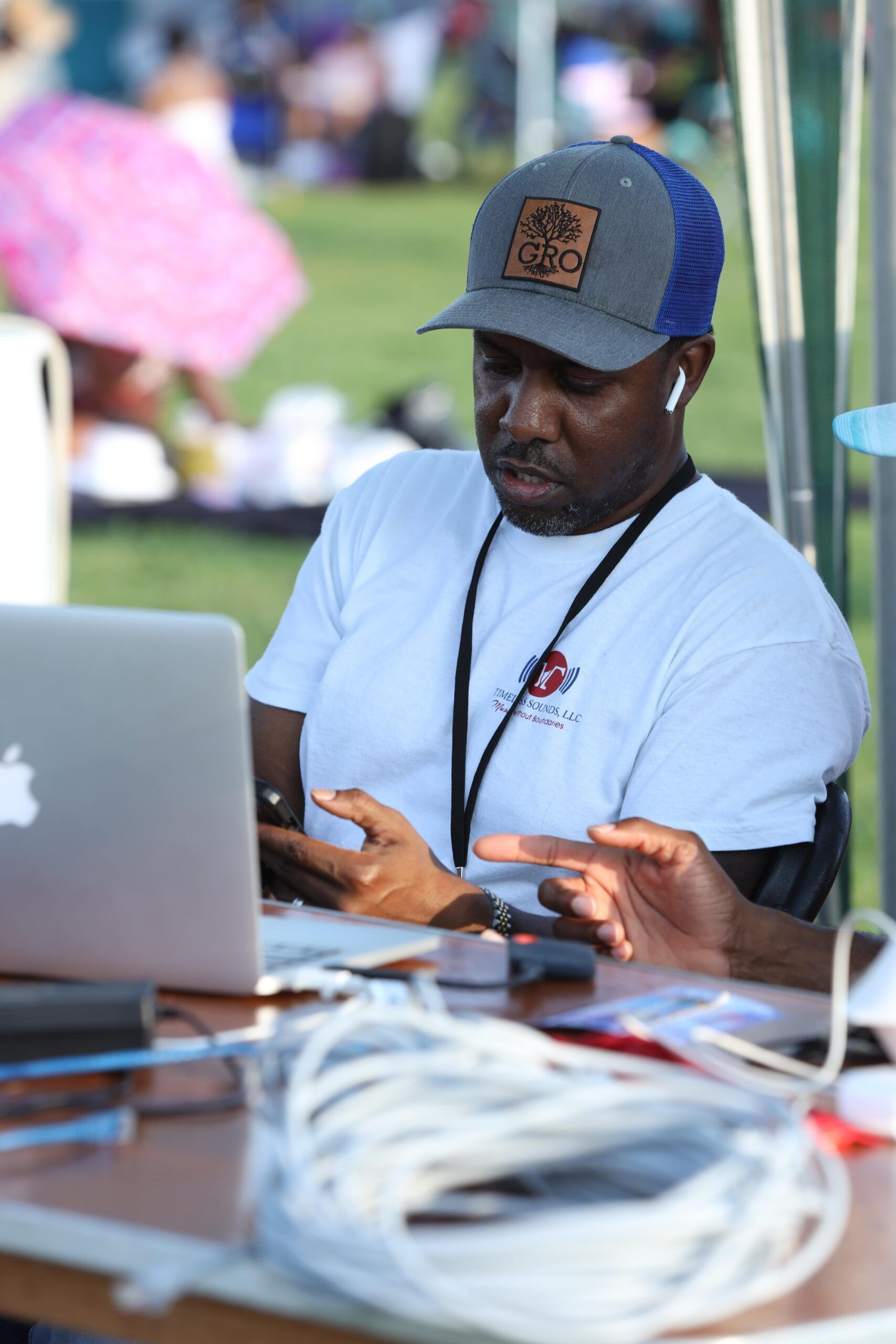 Man using a laptop at an outdoor table, with cables and equipment in the foreground