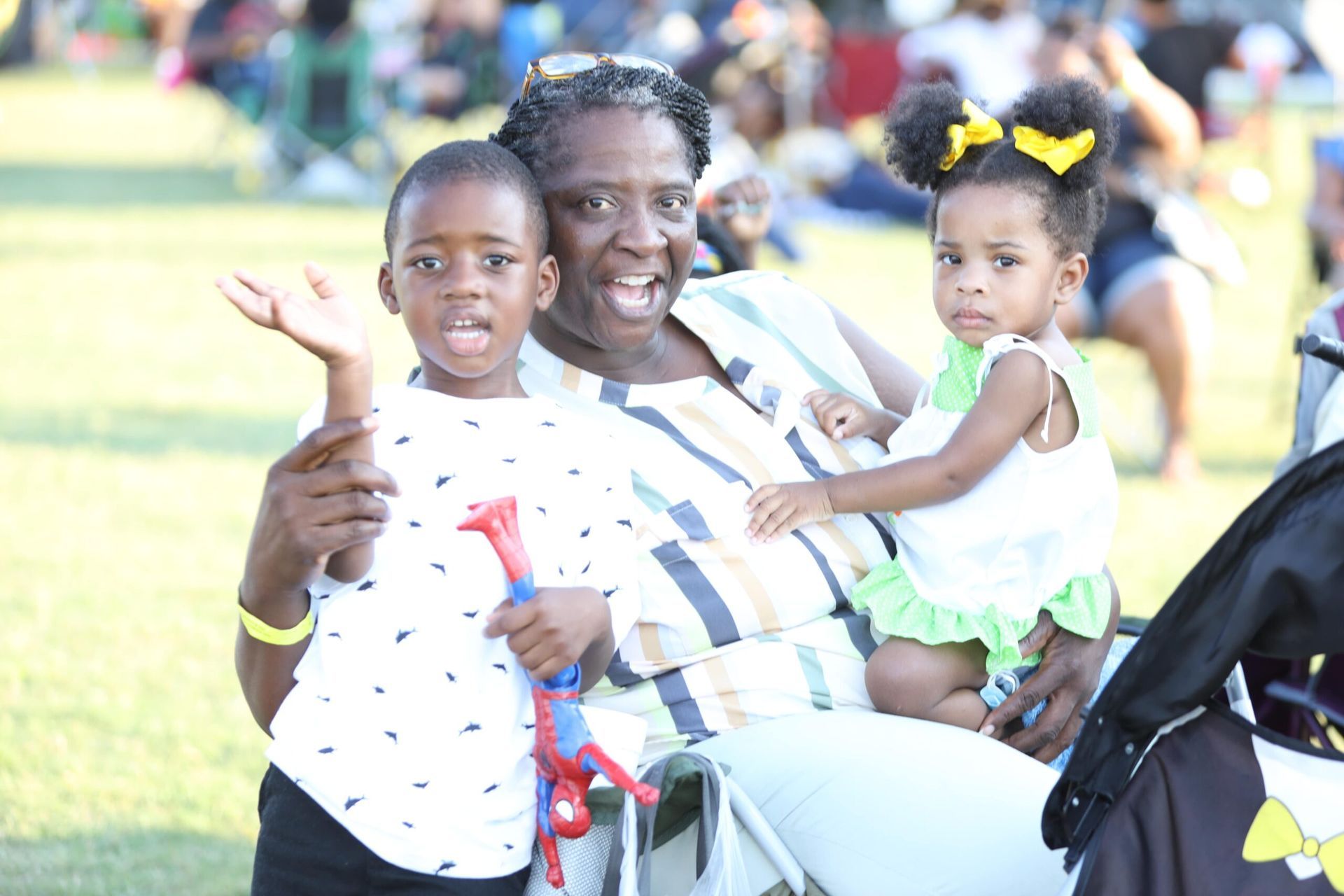 Three people smiling and posing outdoors at a bright event, with a child wearing yellow bows.