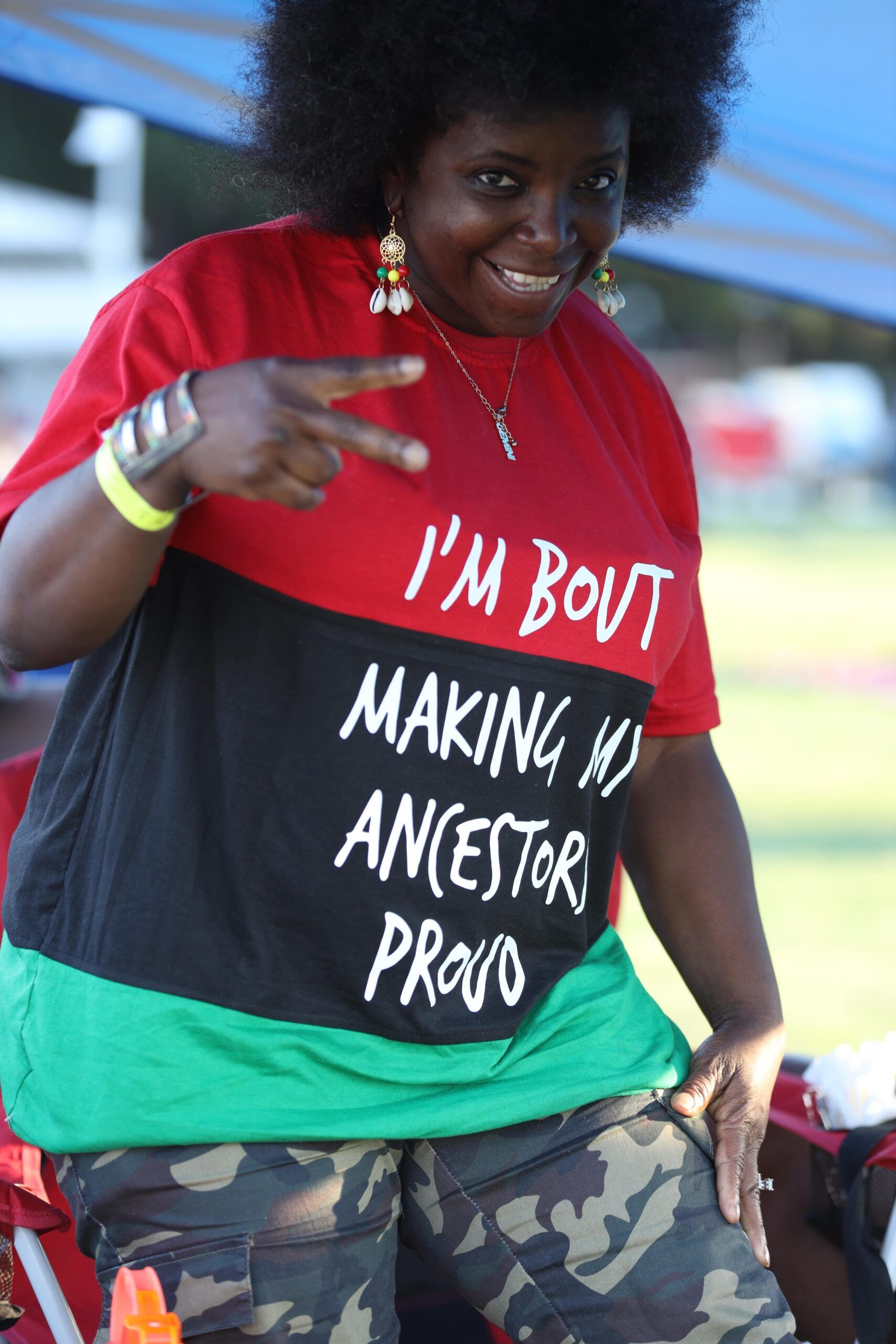 Person in red and black shirt with “I’M BOVI” and “MAKING MY ANCESTOR PROUD” text, posing outdoors