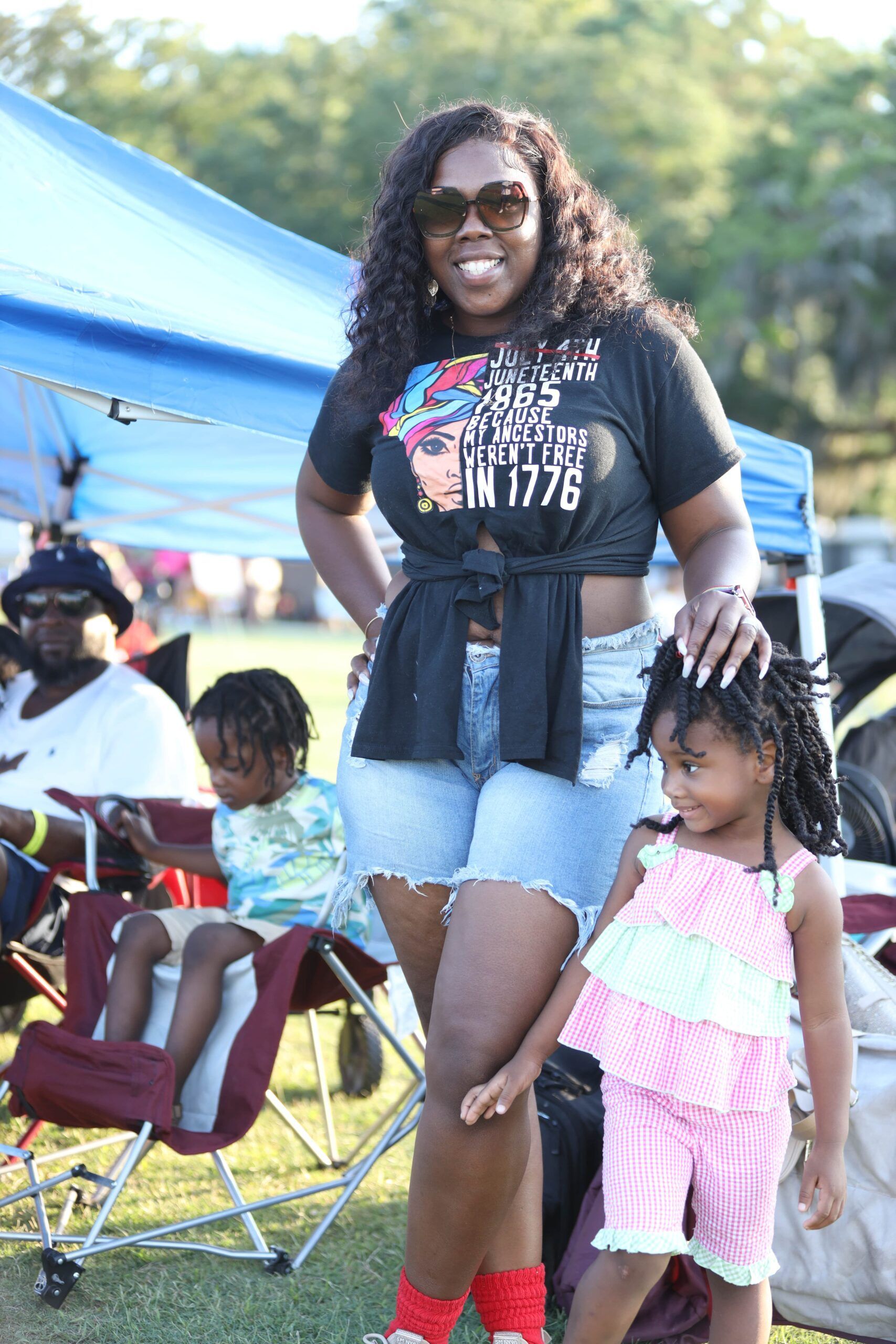 Woman standing outdoors at a community event, with two children beside her under a blue canopy.