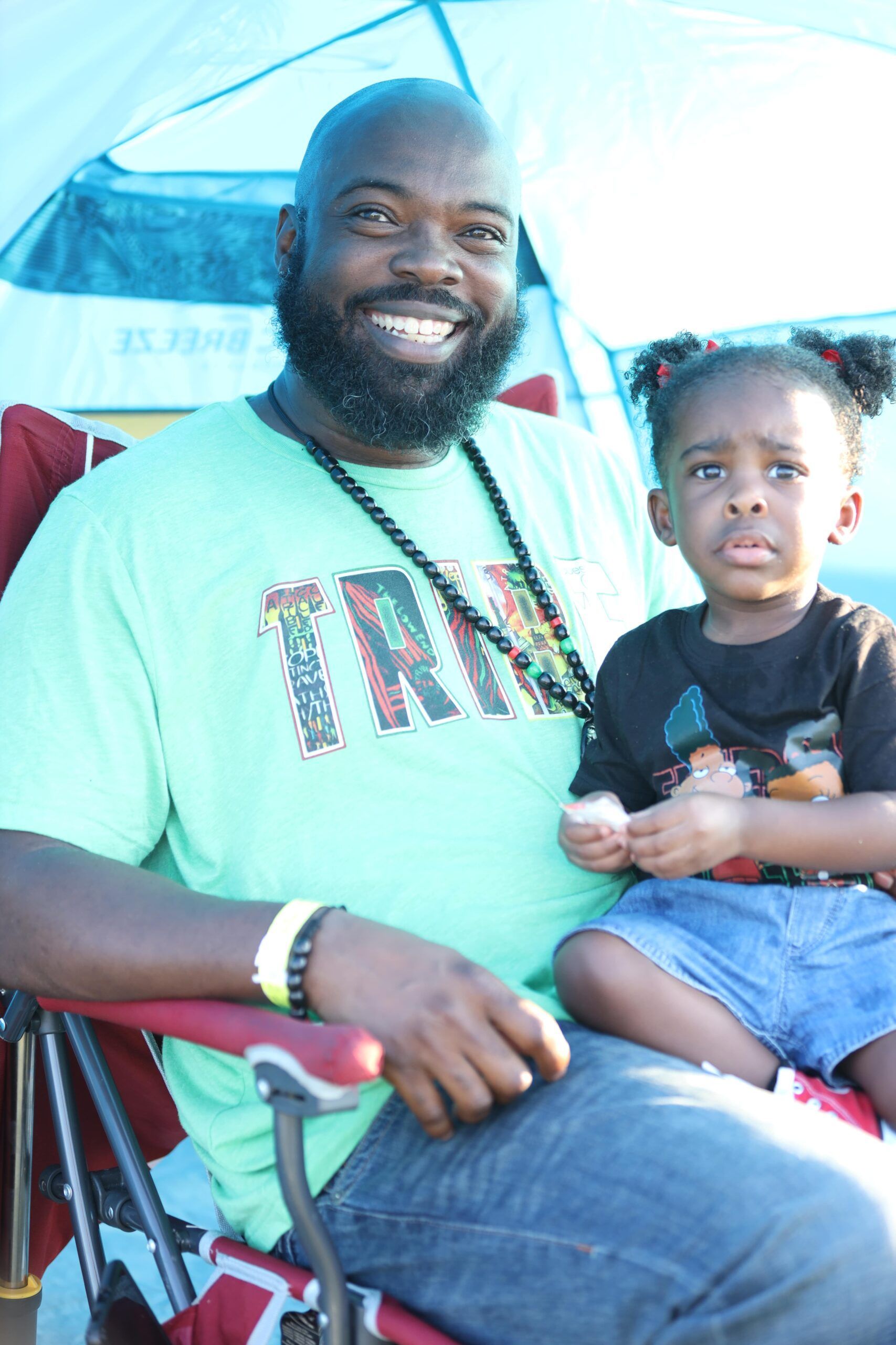 Smiling man in green shirt holding a toddler under a blue-and-white canopy