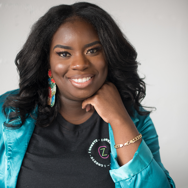 Smiling woman in teal jacket against a light gray background, resting her chin on her hand.