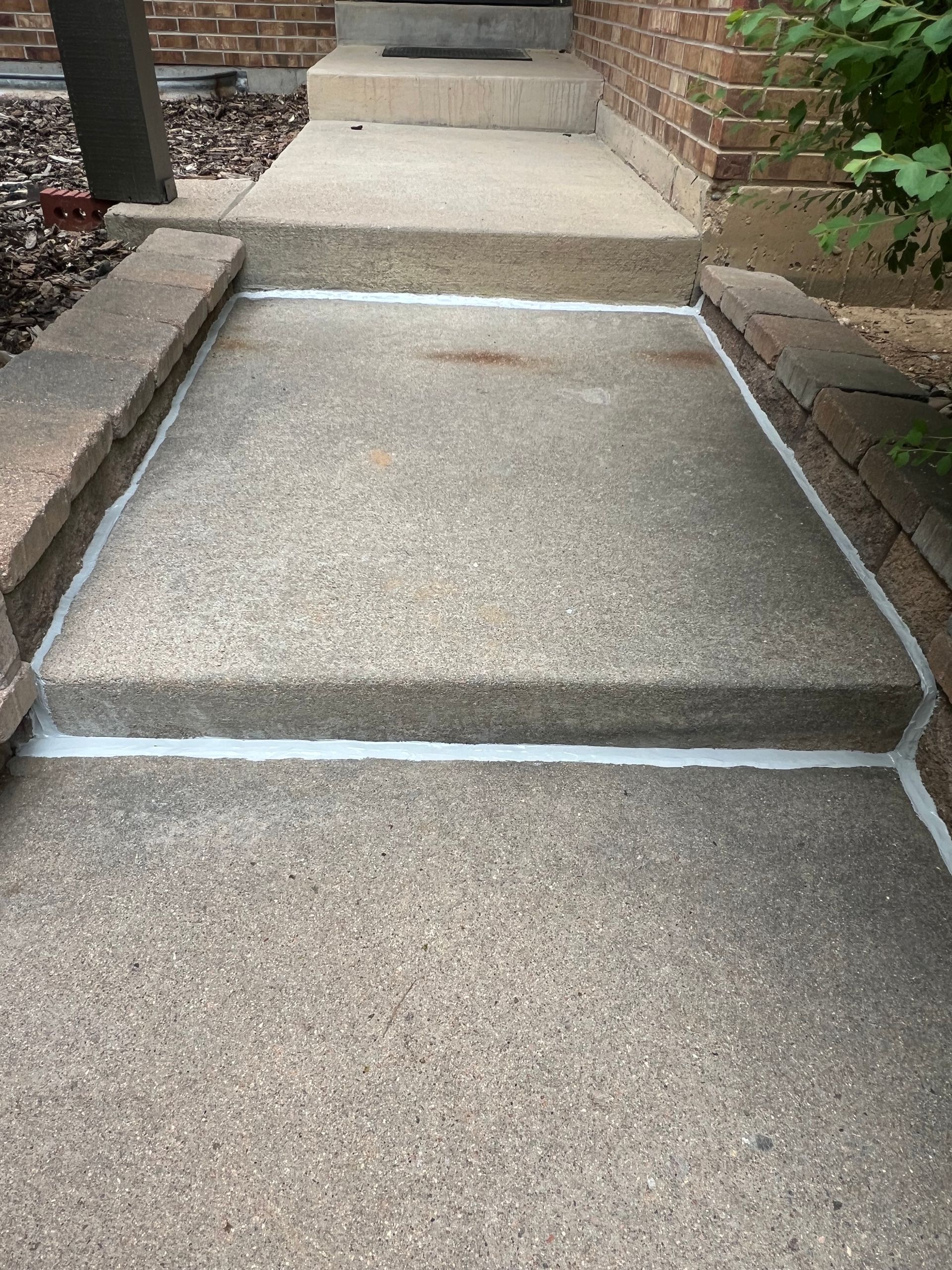 Gloved worker caulking a concrete curb crack with a white sealant gun outdoors