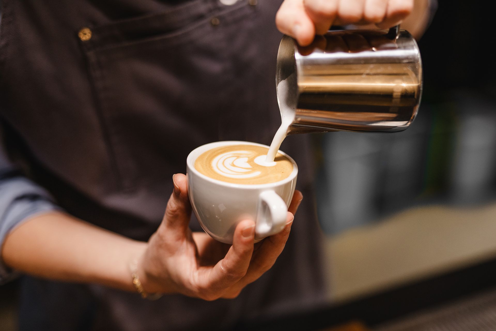 Barista che versa latte montato a vapore in una tazza da caffè bianco, creando una sorta di latte art.