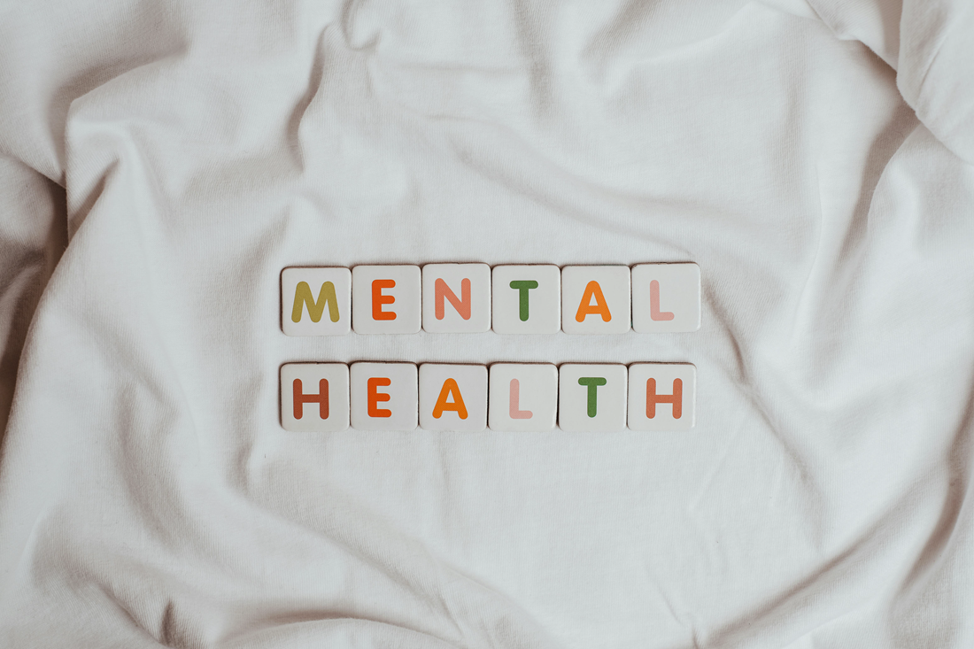 Letter tiles spelling “MENTAL HEALTH” on a white cloth background.