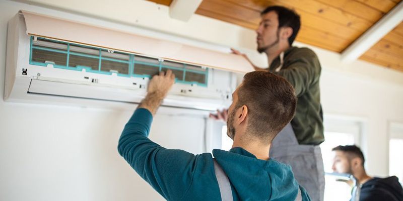 Two technicians installing a white wall-mounted air conditioner indoors