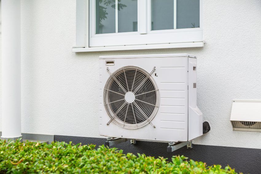 Outdoor air conditioning unit mounted under a window on a white house wall
