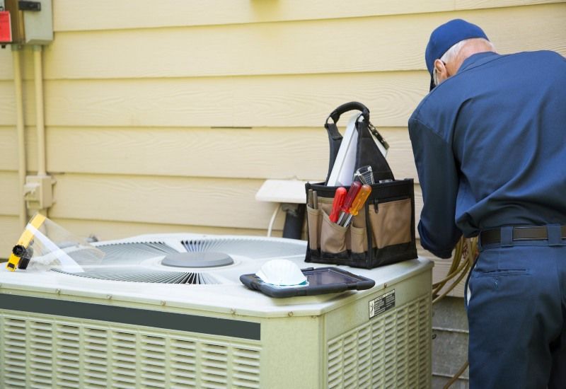 Technician working on an outdoor HVAC unit beside a house wall