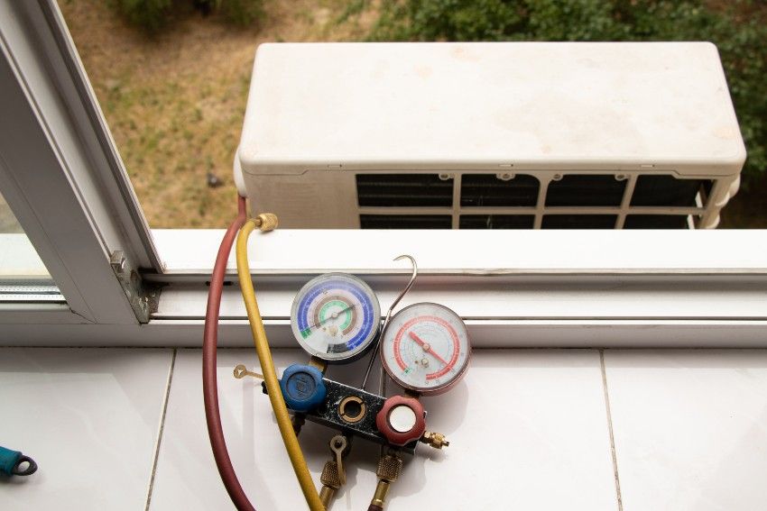 HVAC pressure gauges and hoses on a windowsill facing an outdoor AC unit