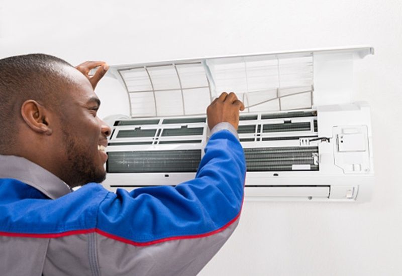 Technician cleaning a wall-mounted air conditioner with the cover open