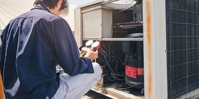 Technician inspecting an outdoor air conditioner unit with a flashlight and tools