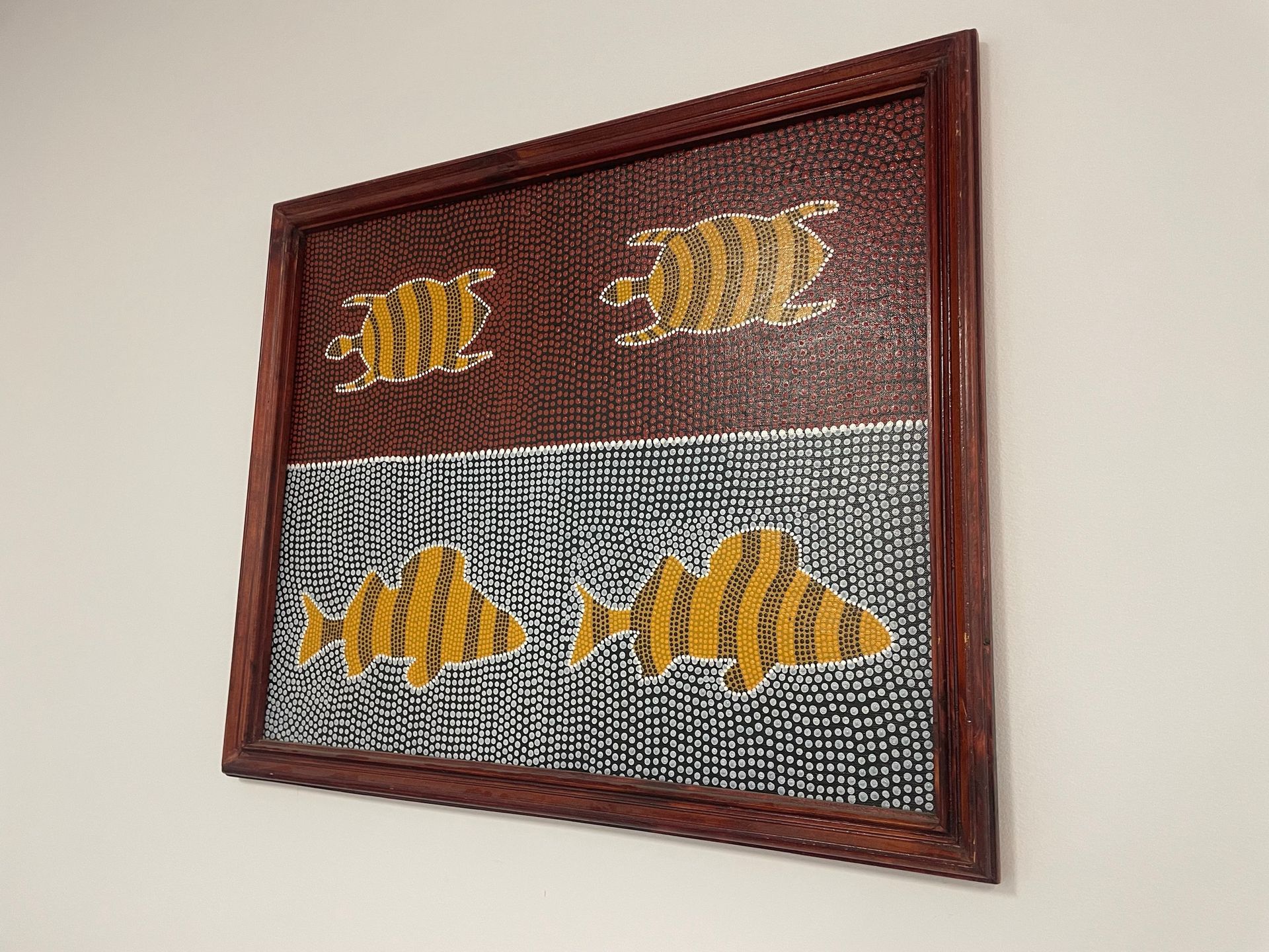 A painting of fish is hanging on a wall in a wooden frame.