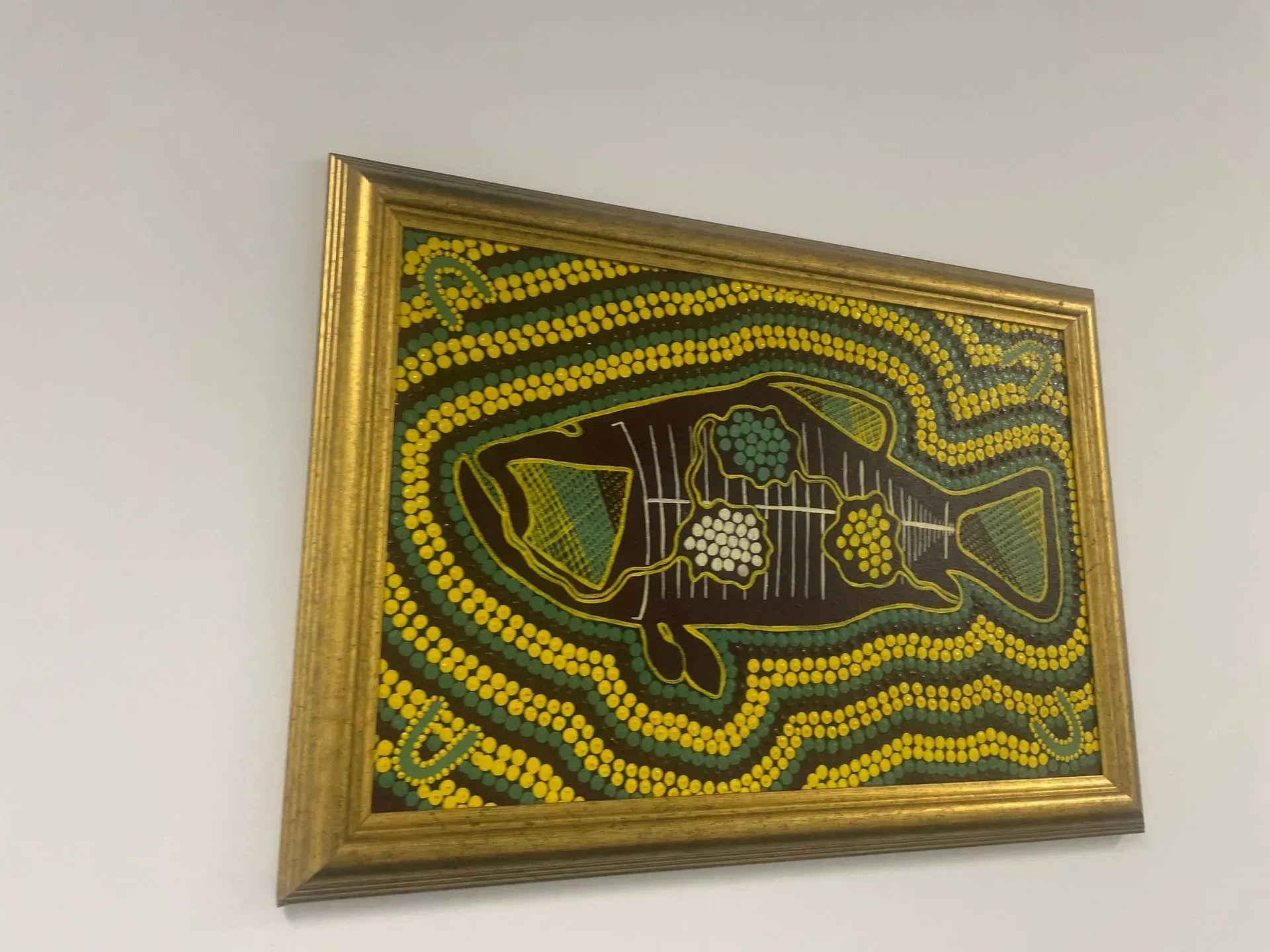 A painting of a fish is hanging on a white wall.