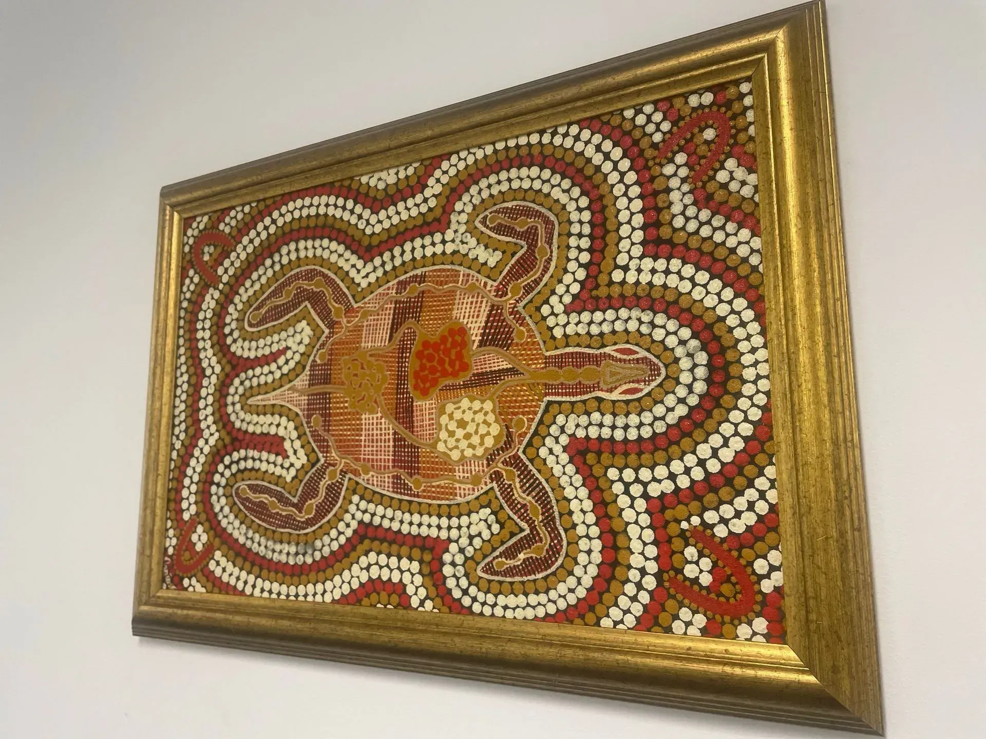 A picture in a gold frame is hanging on a white wall.