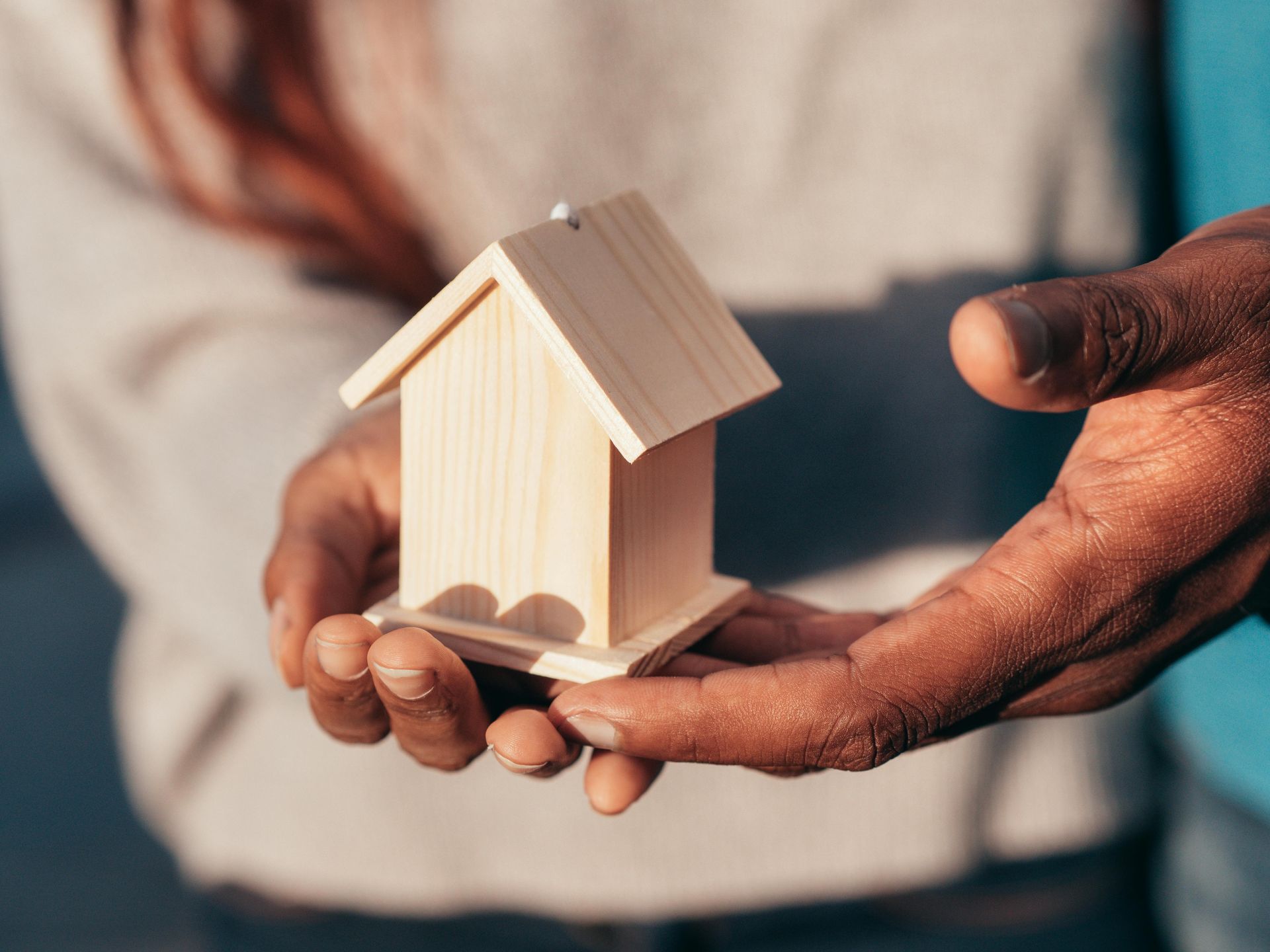 Hands holding a wooden house model, symbolizing the safe community living and holistic support services offered by Plan and Grow.