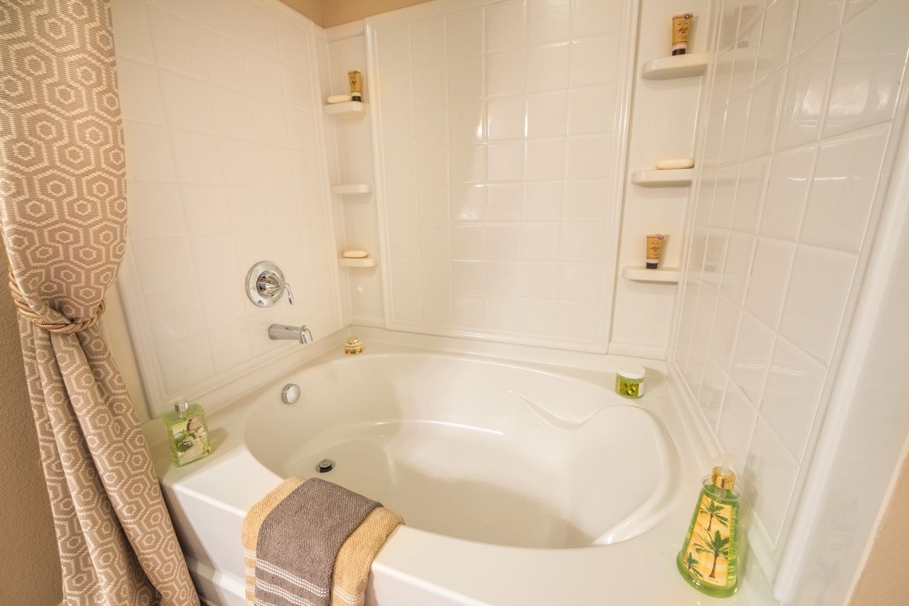 White bathtub with built-in shower surround and tiled walls, beige patterned curtain.