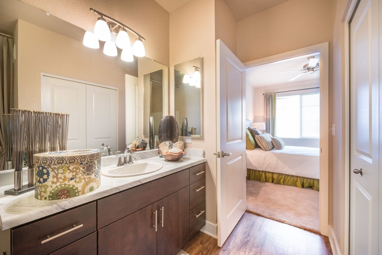 View of a bathroom vanity with a double sink, marble countertop, and doorway to a bedroom.