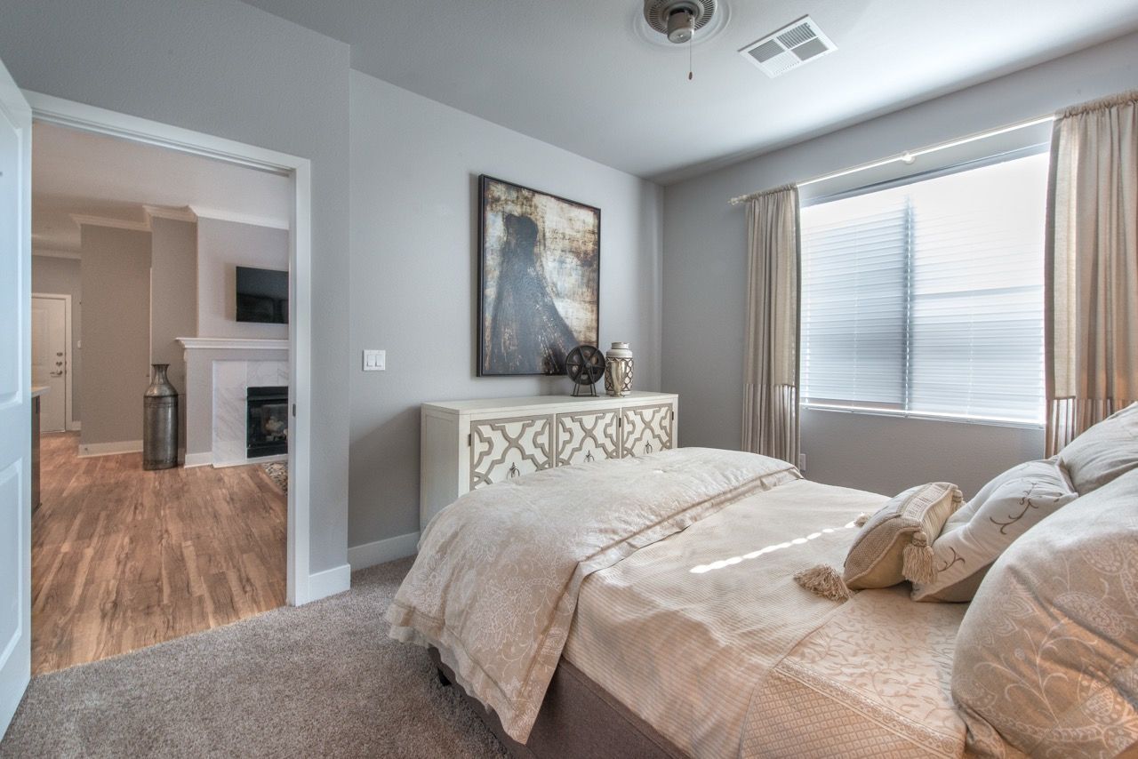 Bedroom with a large window, beige bedding, and a decorative white dresser.