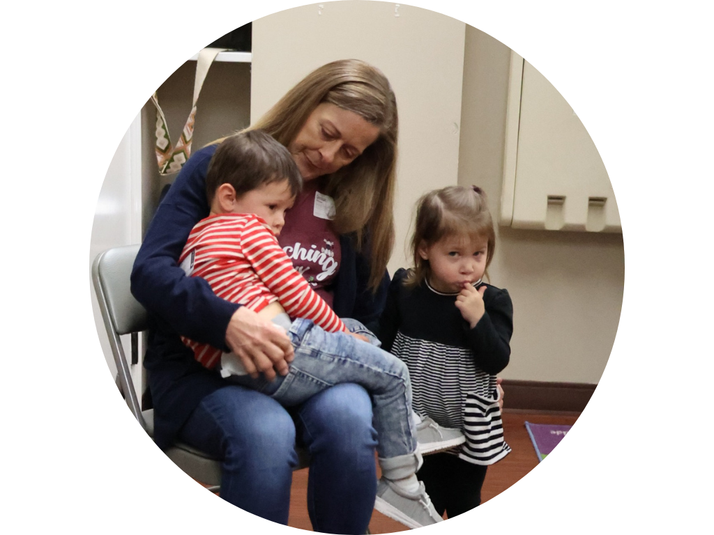 A woman is sitting in a chair holding two children.