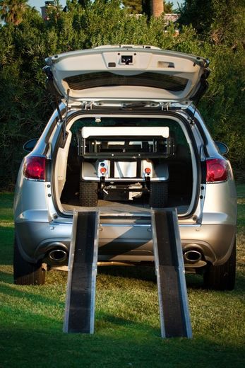 A silver car with the trunk open and ramps in front of it and a Cricket inside