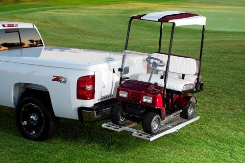 A golf cart is attached to the back of a white truck.