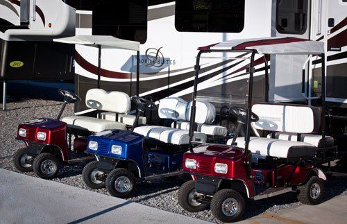 Three golf carts are parked in front of a rv.