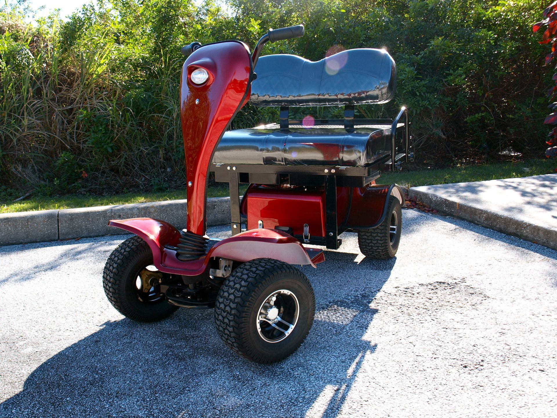 A red golf cart with a blue seat is parked on gravel.