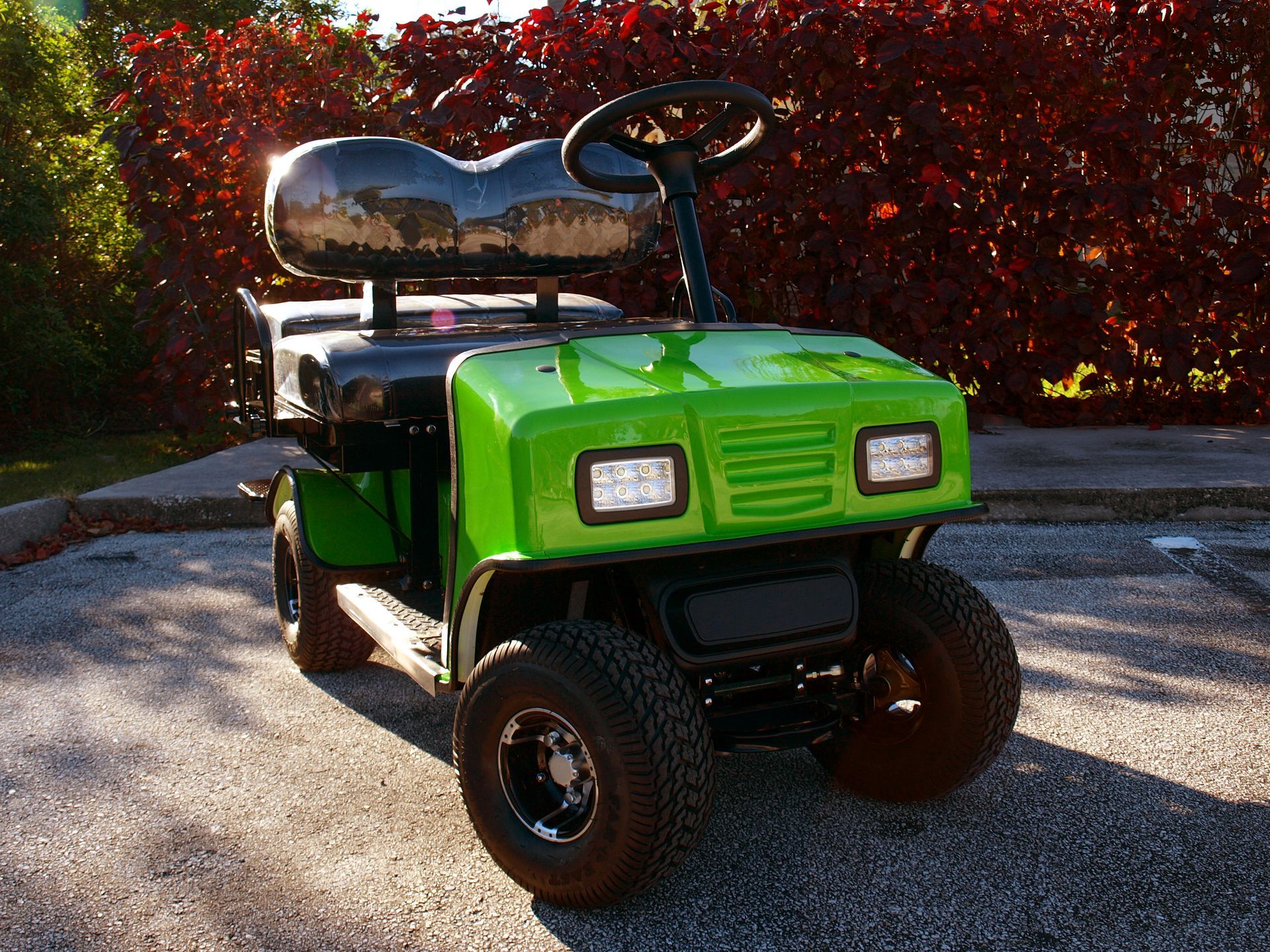 A green golf cart is parked in a parking lot.
