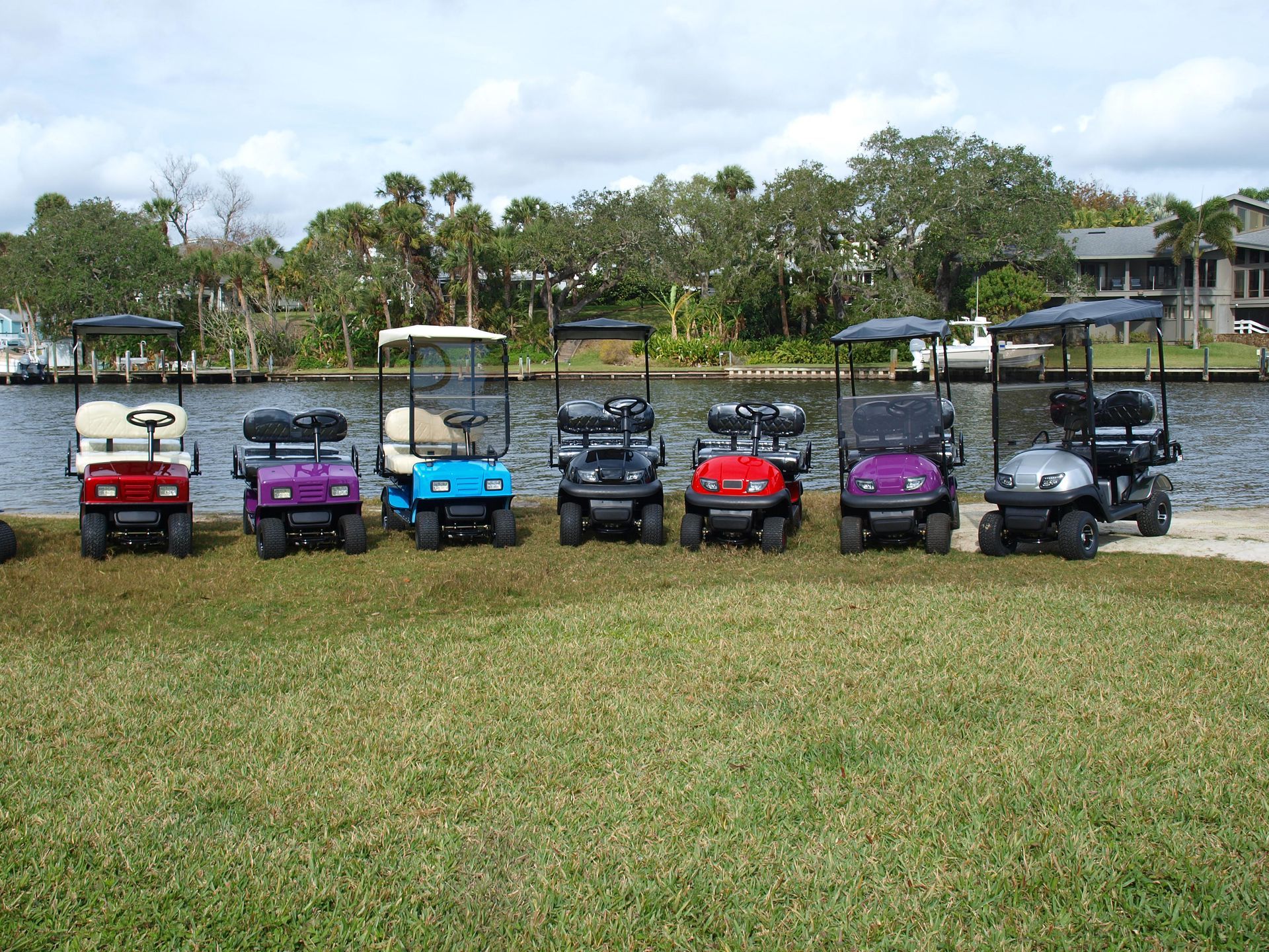 A row of golf carts are parked in a grassy area near a body of water.