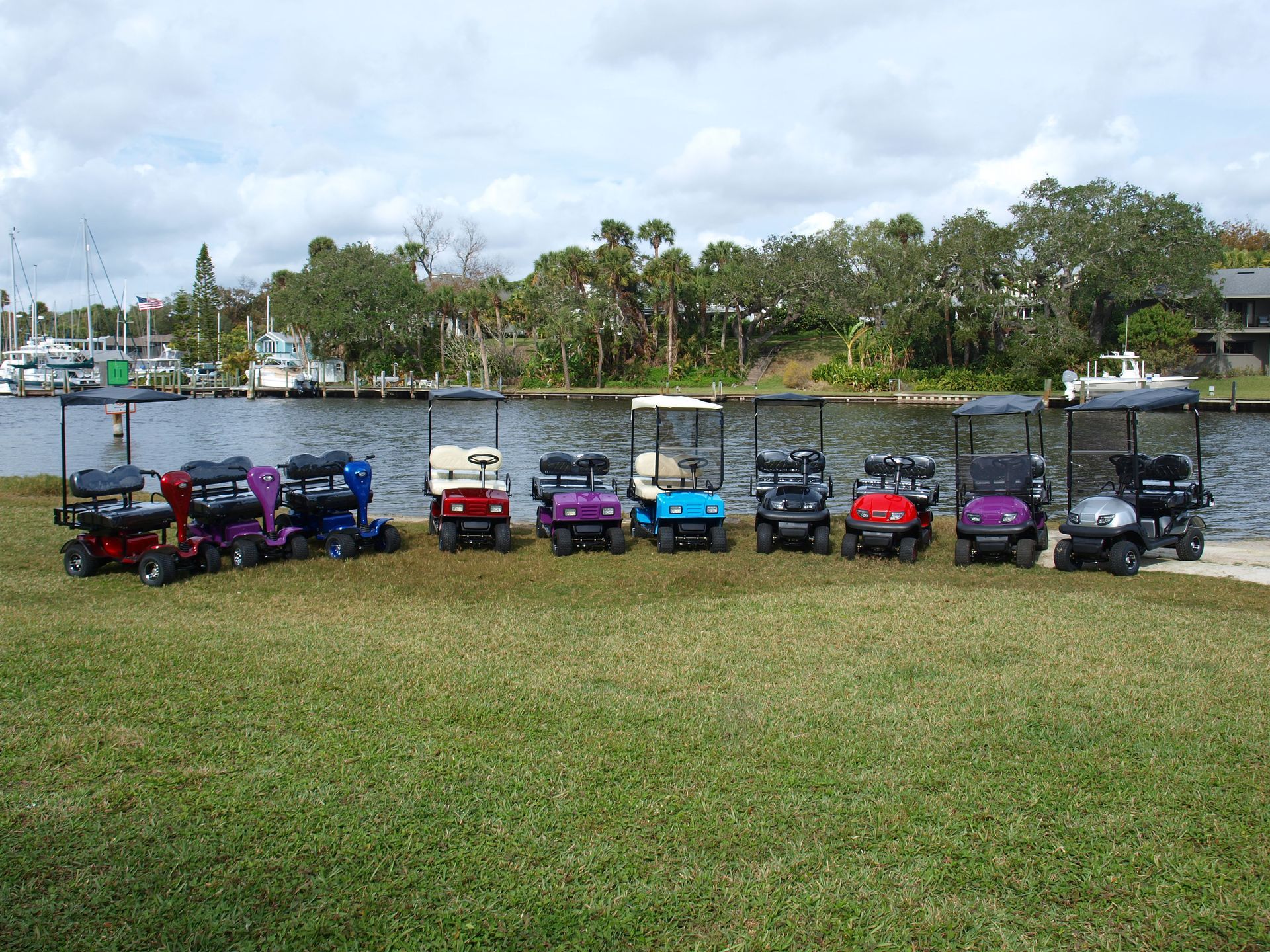A row of golf carts are parked in a grassy area near a body of water.