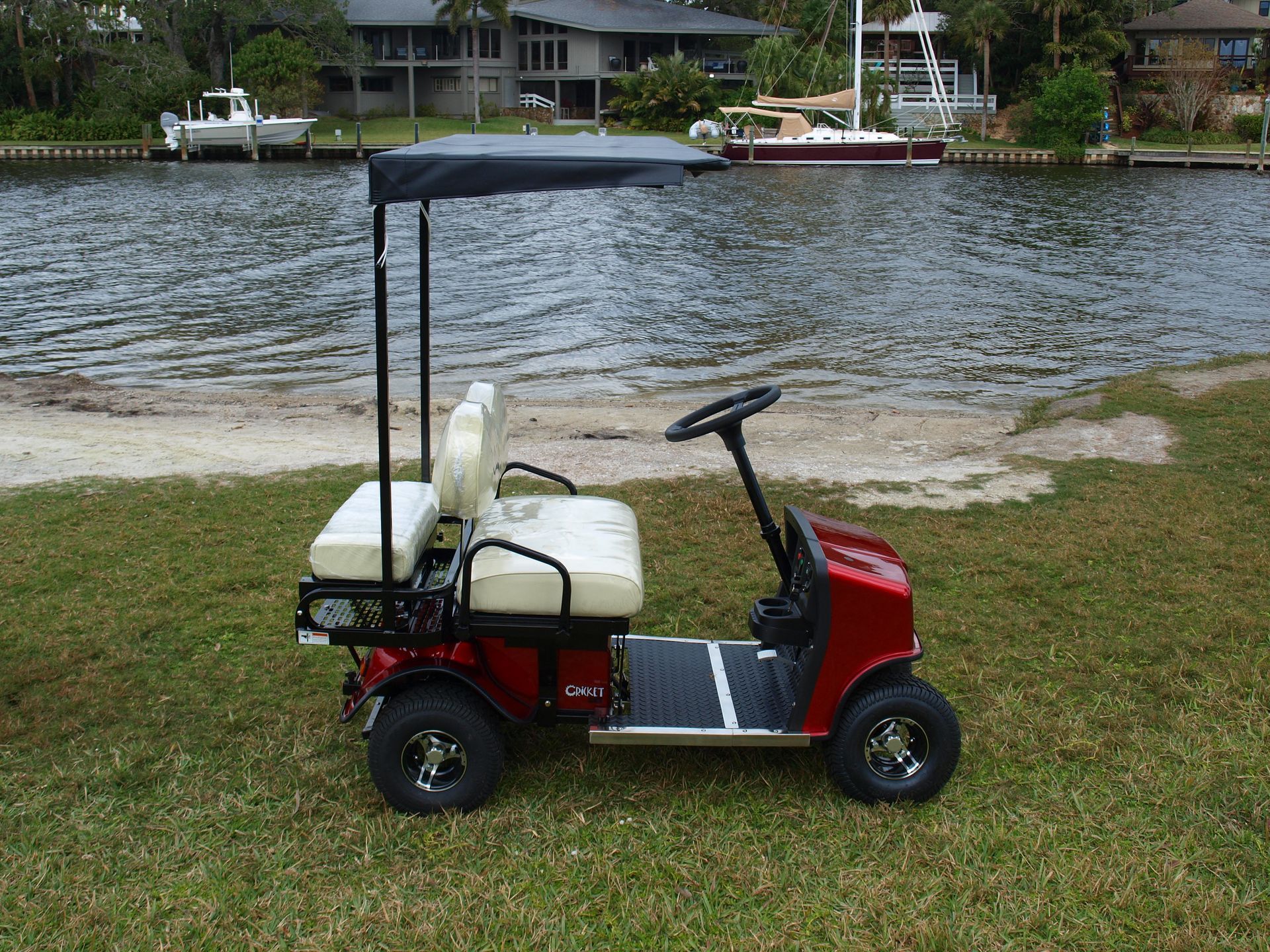 A red golf cart with a canopy is parked next to a body of water.