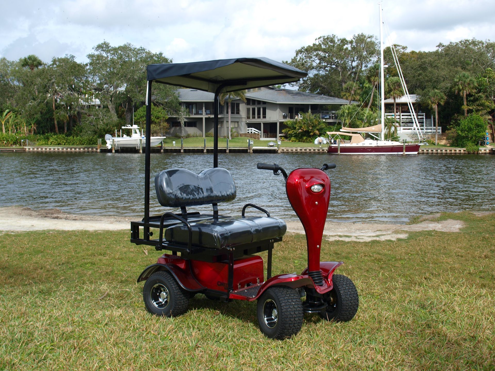 A red Cricket golf cart with a canopy is parked next to a body of water