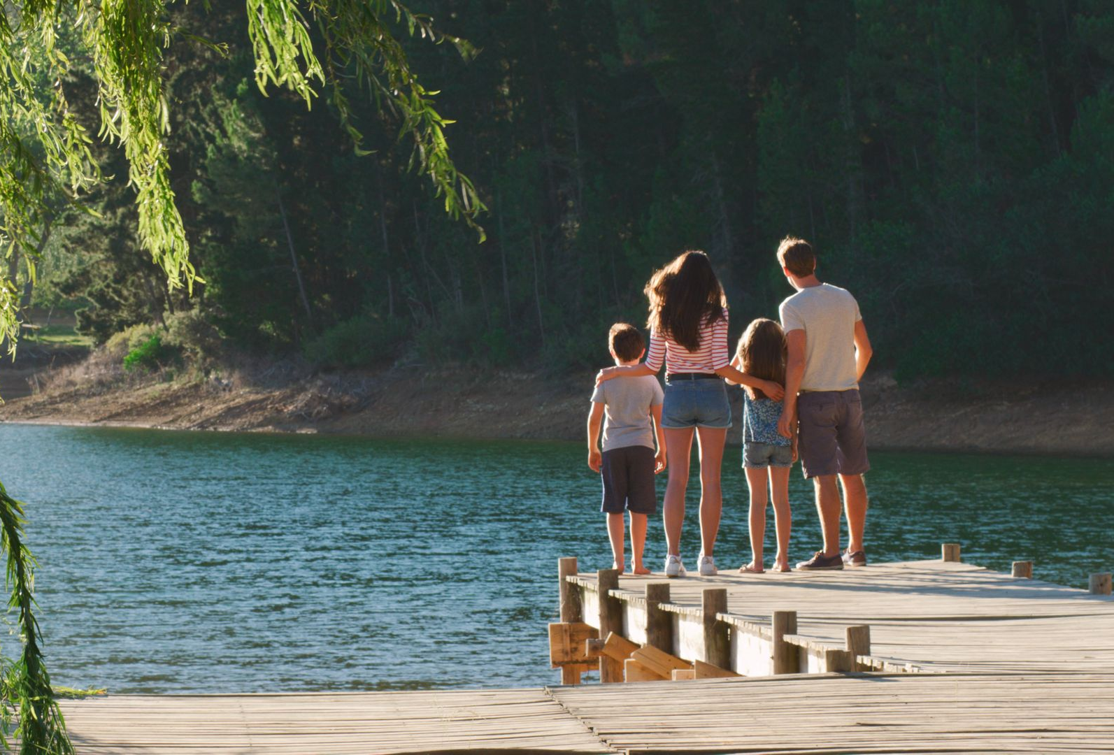 Family standing on a wooden dock, looking out at a lake.