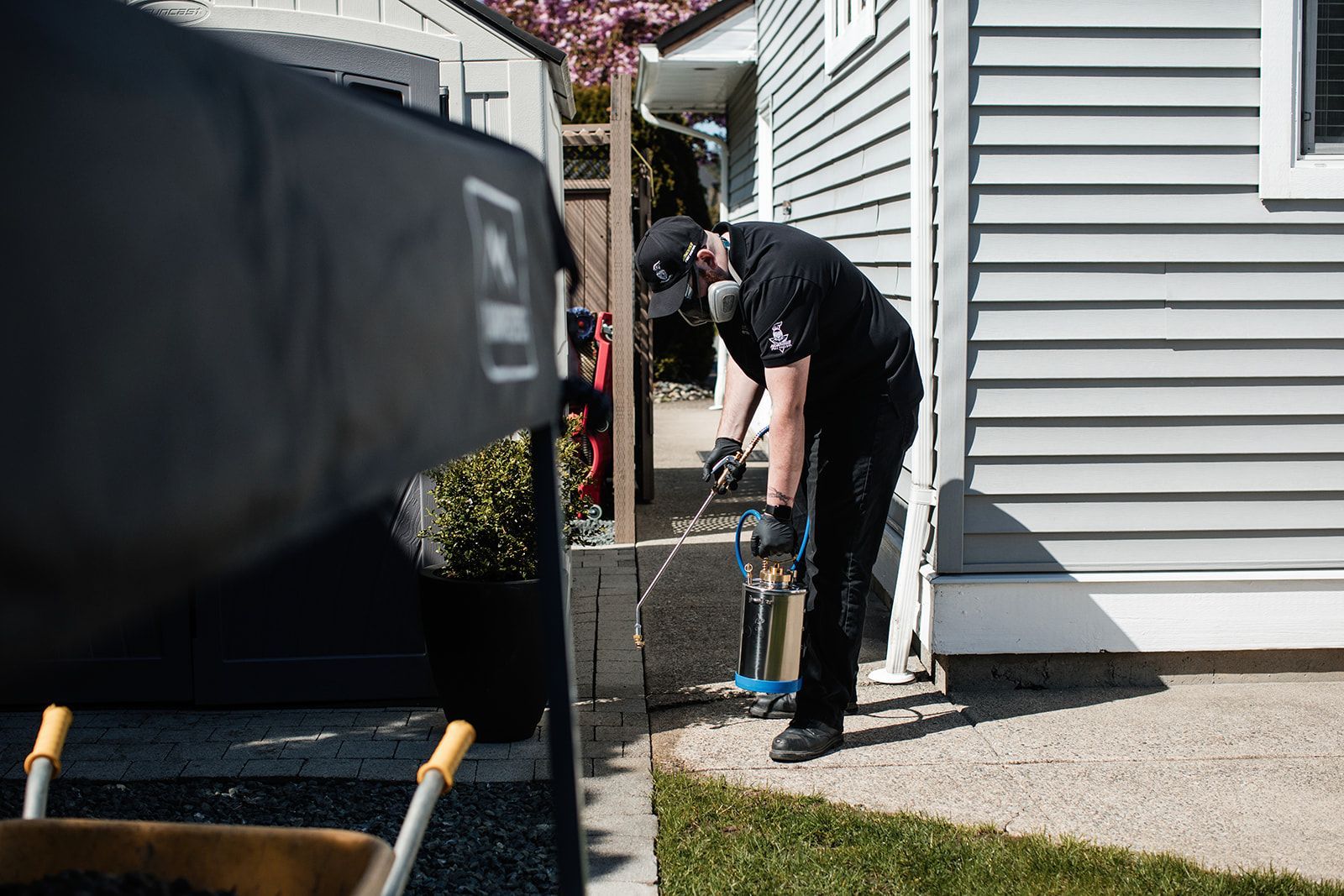 Person using a pressure washer beside a house next to a large black trailer.