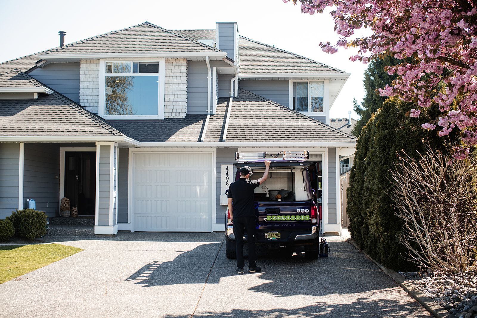 Person standing by a utility cart in front of a two-story suburban house with a garage