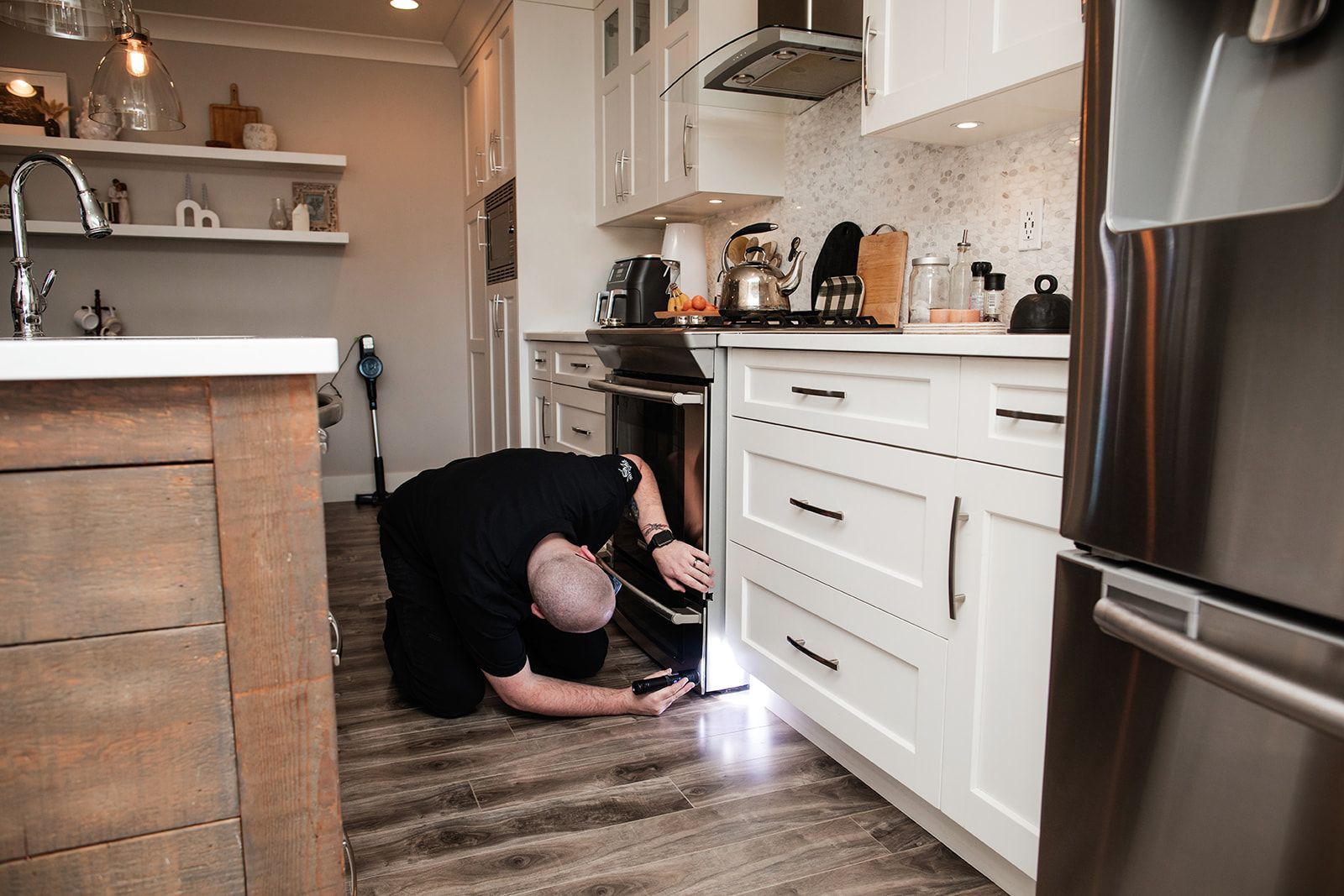A man is kneeling on the floor in a kitchen looking into an oven.