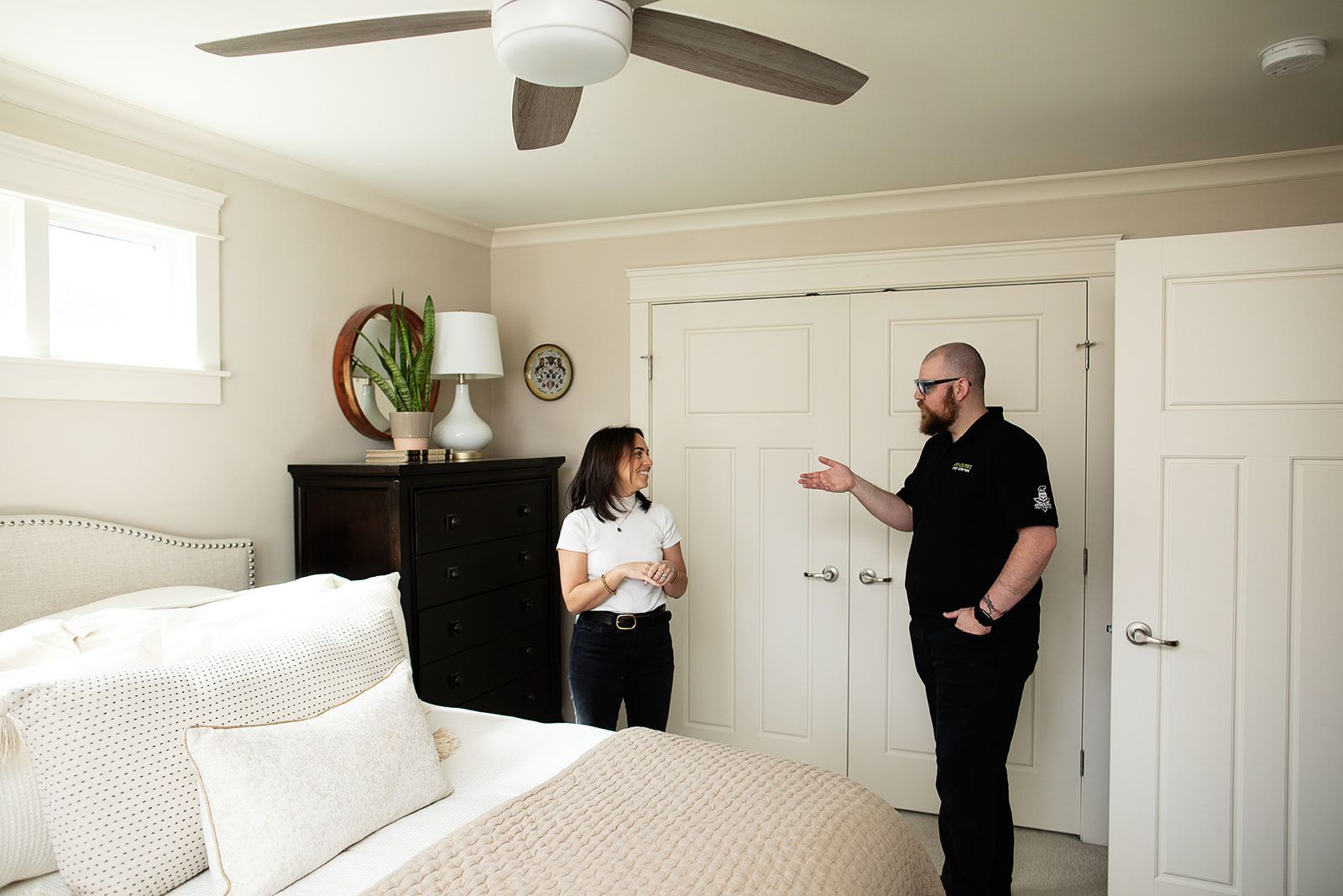 A man and a woman are standing in a bedroom with a ceiling fan.