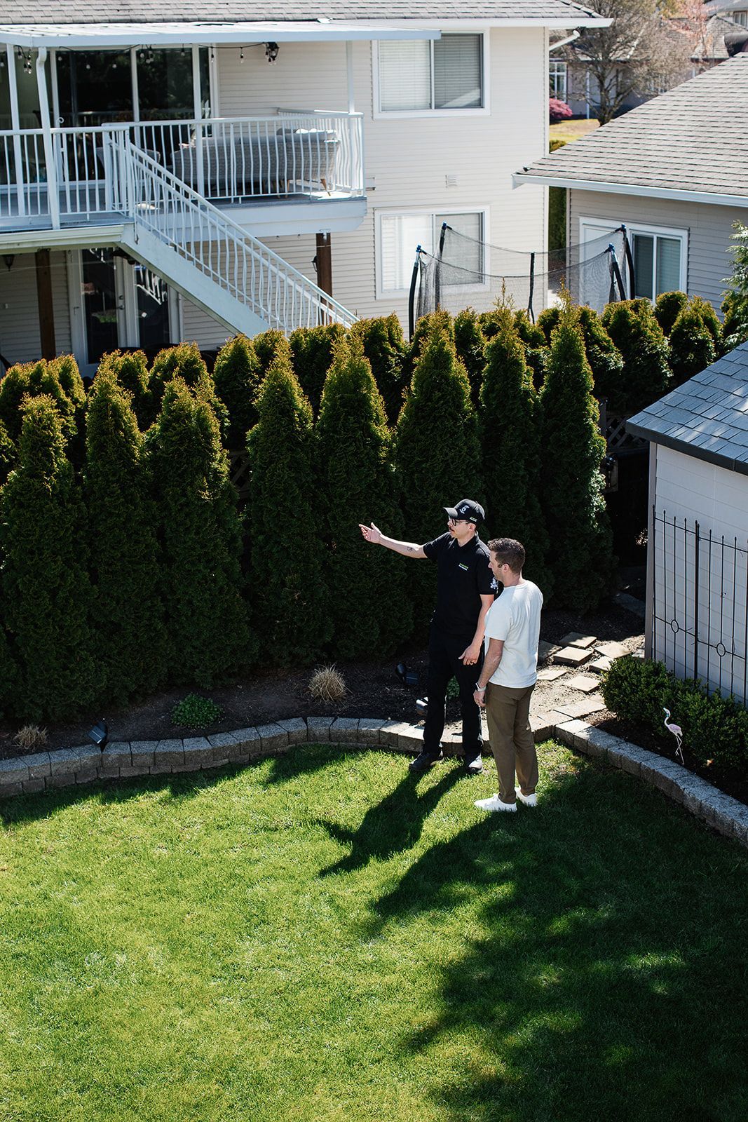 Two men are standing on a lush green lawn in front of a house.