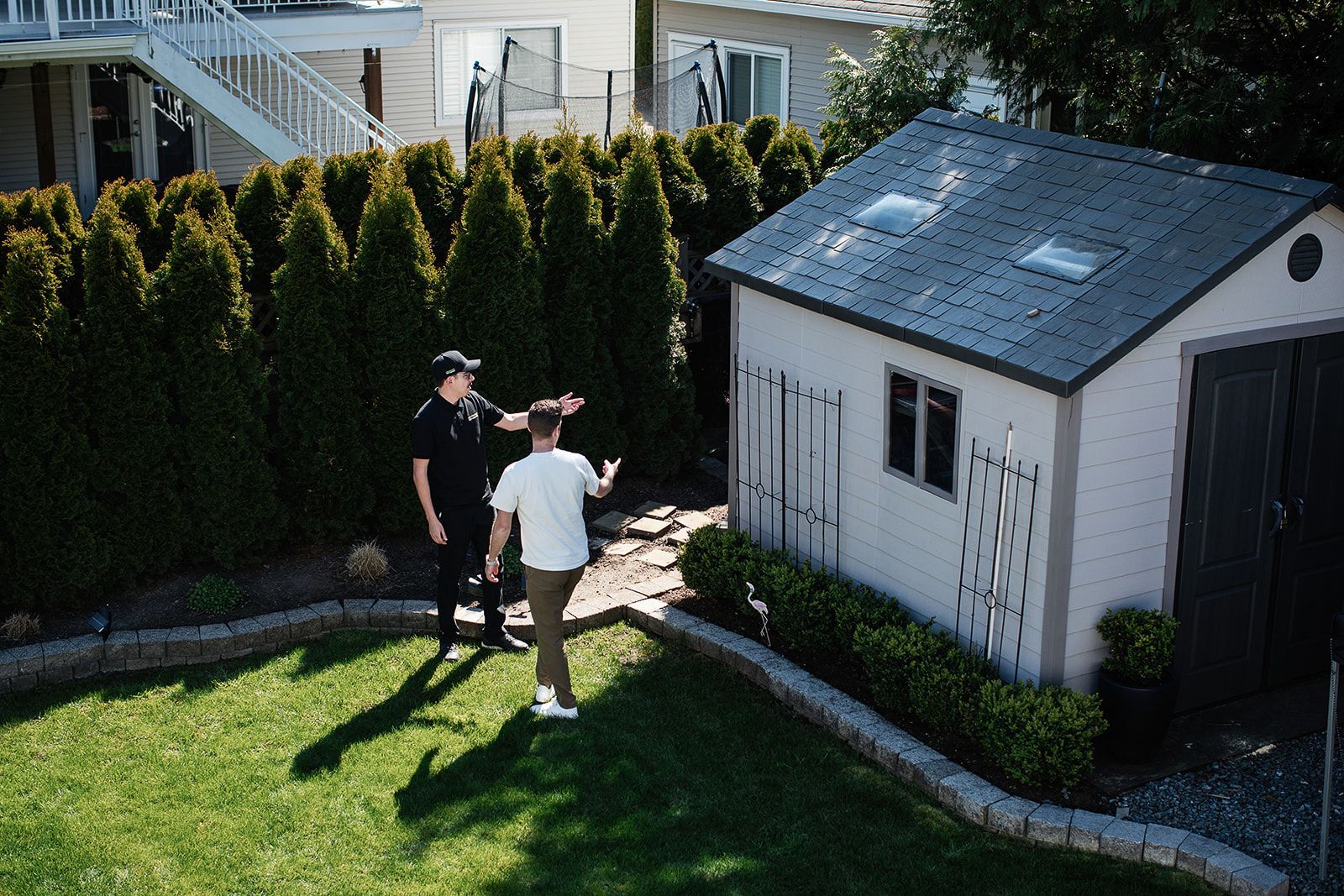 Two men are standing in front of a shed in a backyard.